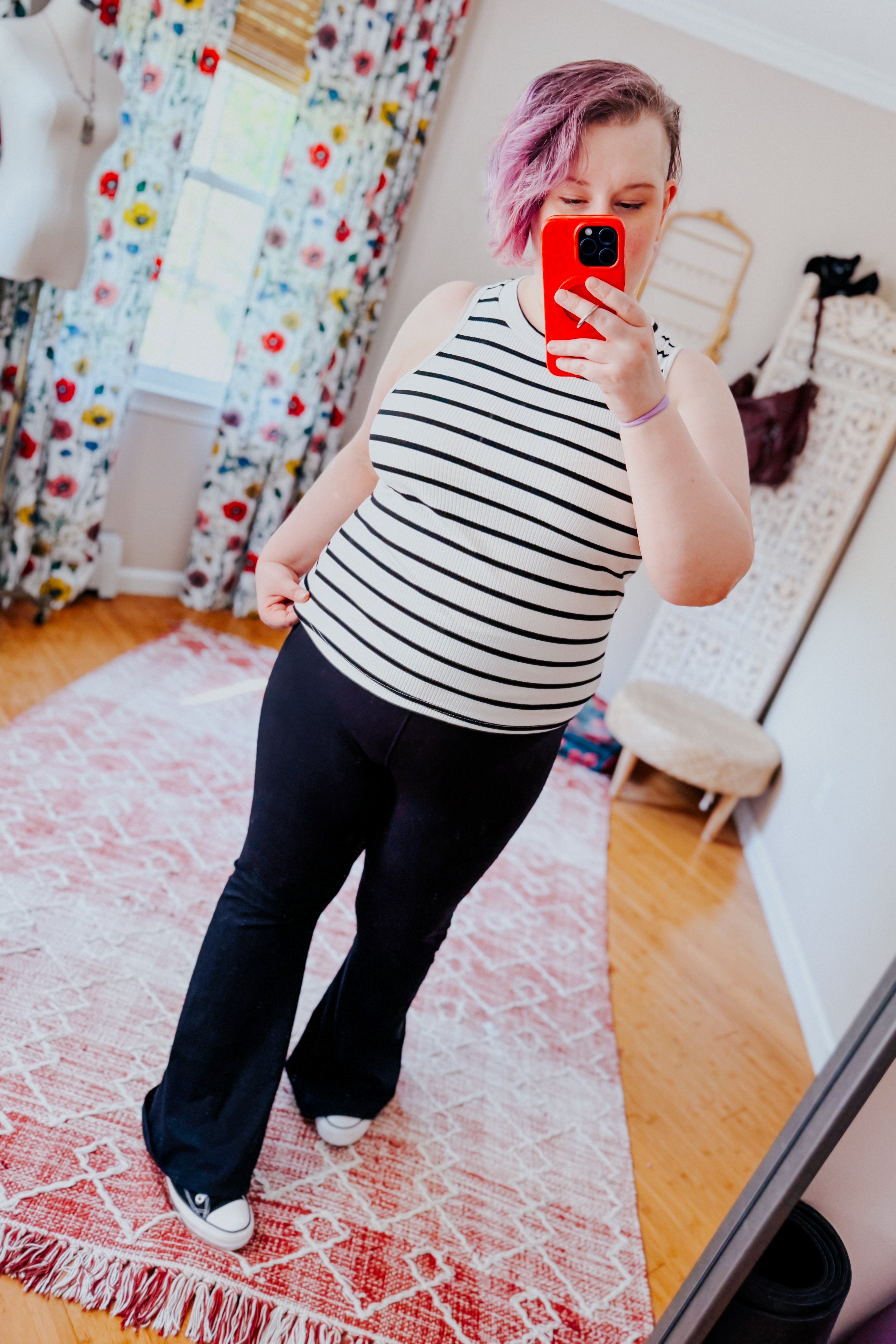 Woman with pink hair wearing a striped sleeveless halter tank paired with black flared pants and sneakers indoors