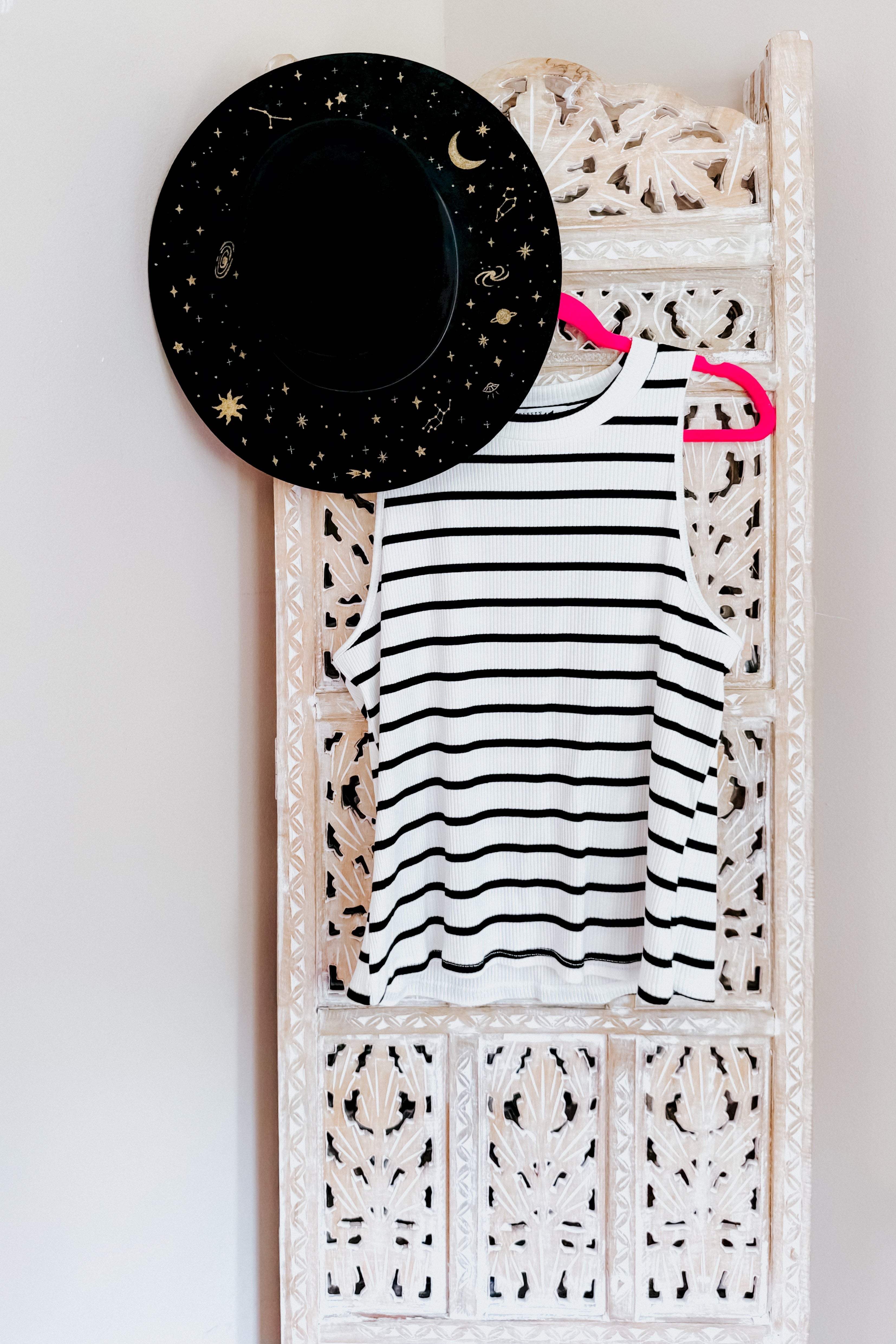 Striped ribbed halter tank in ivory and black hanging on ornate carved wooden panel with black celestial hat above