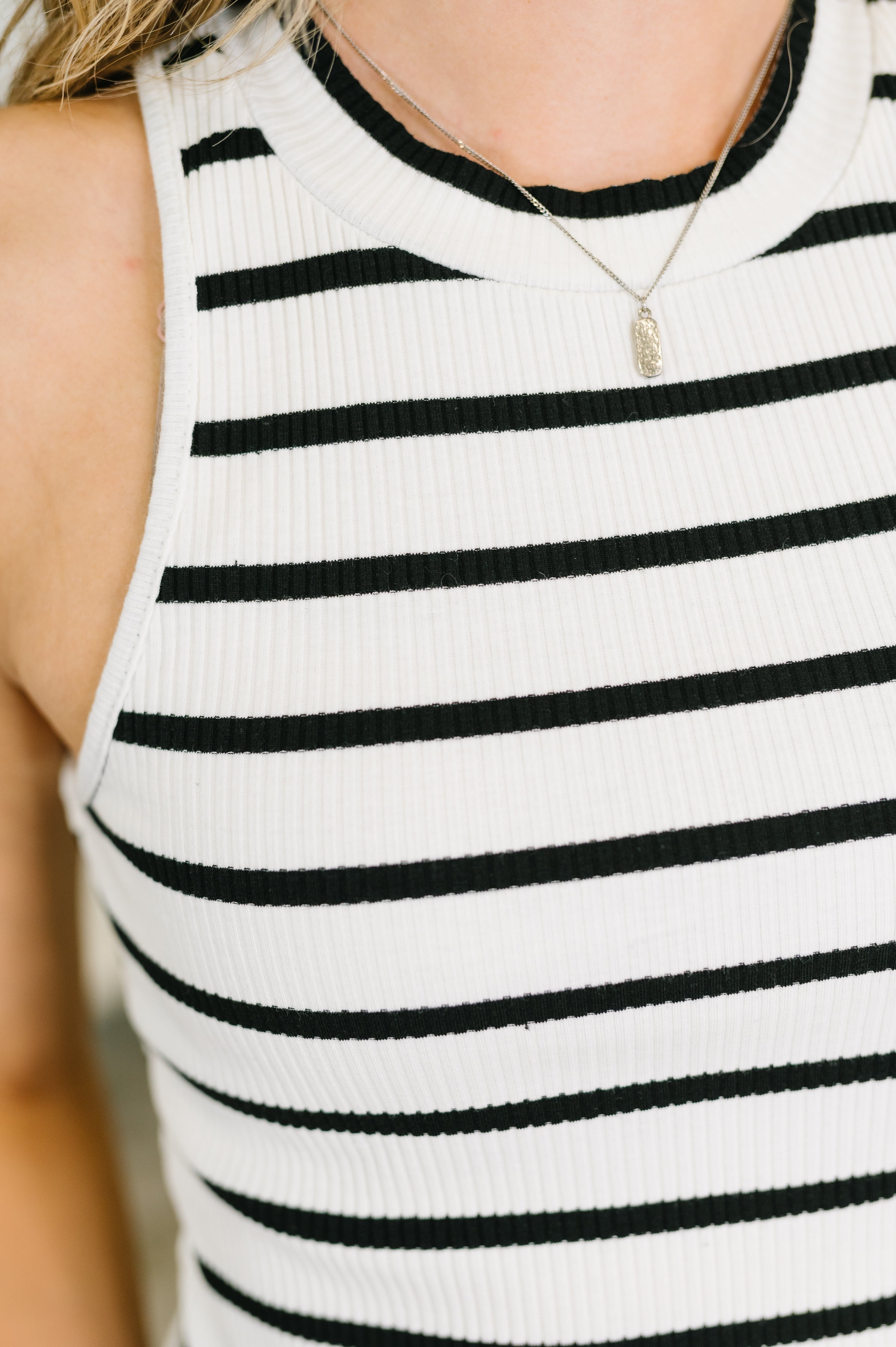 Close-up of ribbed ivory halter tank with black stripes and delicate silver pendant necklace on woman
