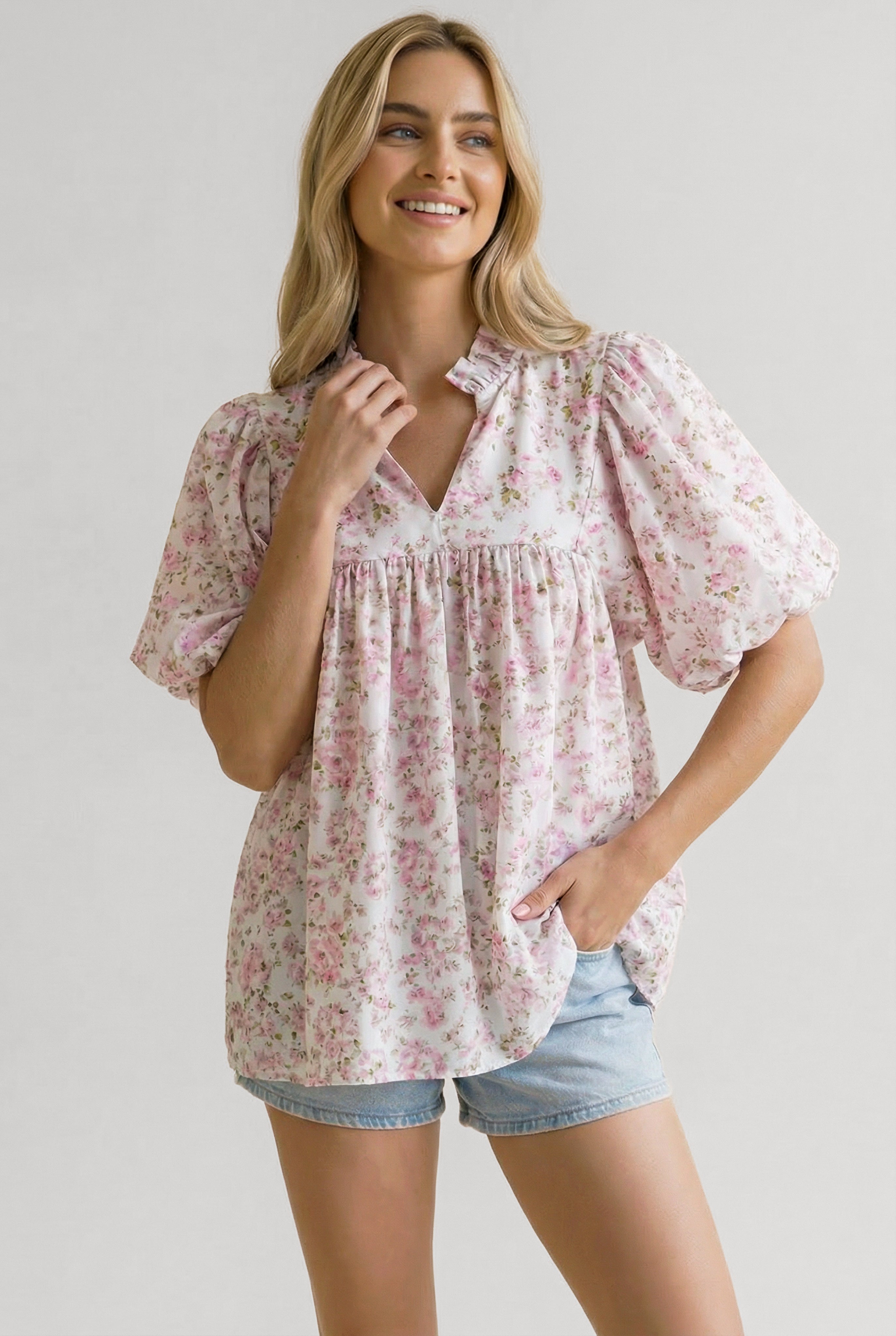 Woman wearing a loose pink floral blouse with puffed short sleeves and a ruffled V-neck paired with light denim shorts