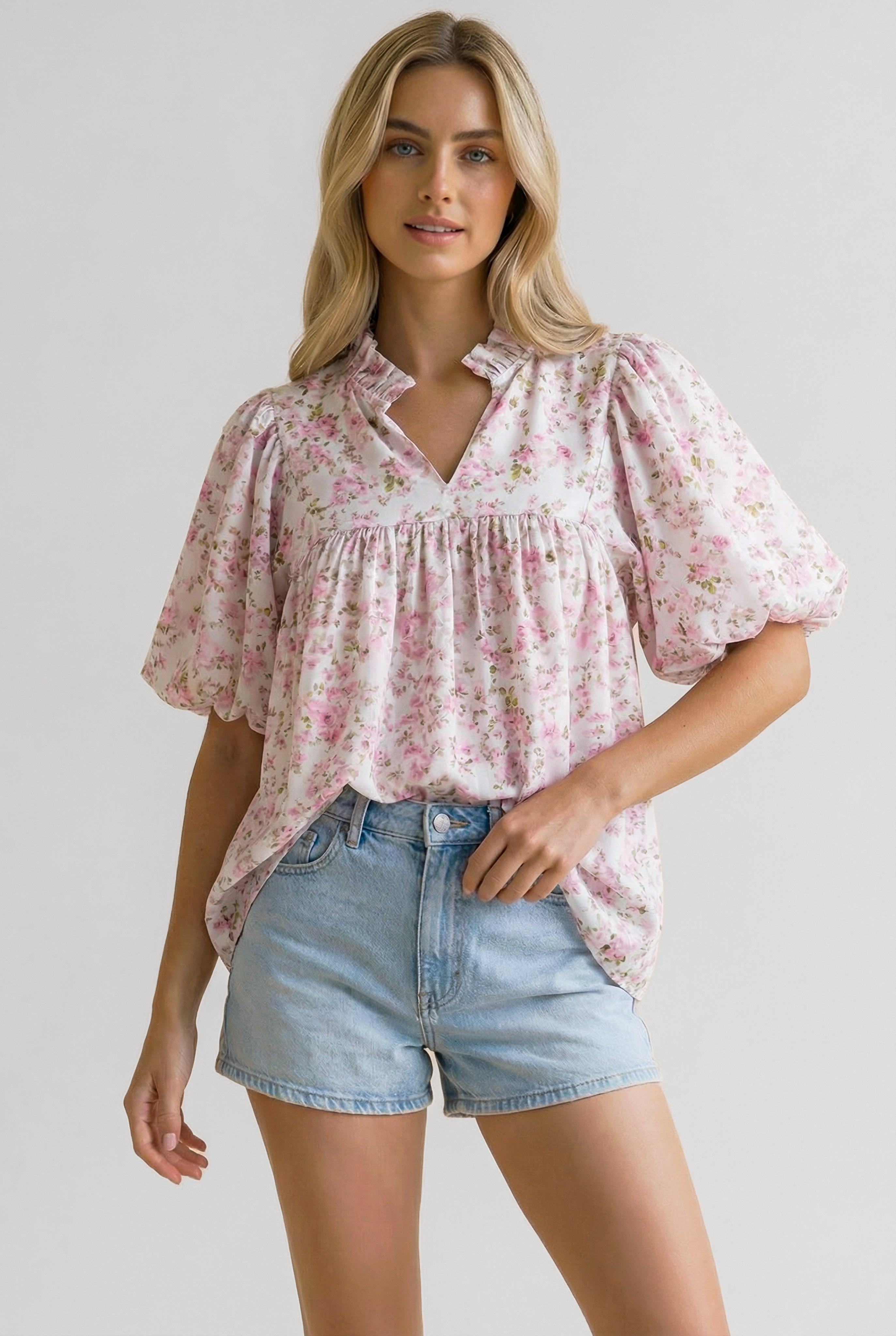 Woman wearing a pink floral blouse with puffed short sleeves and a gathered empire waist paired with light denim shorts