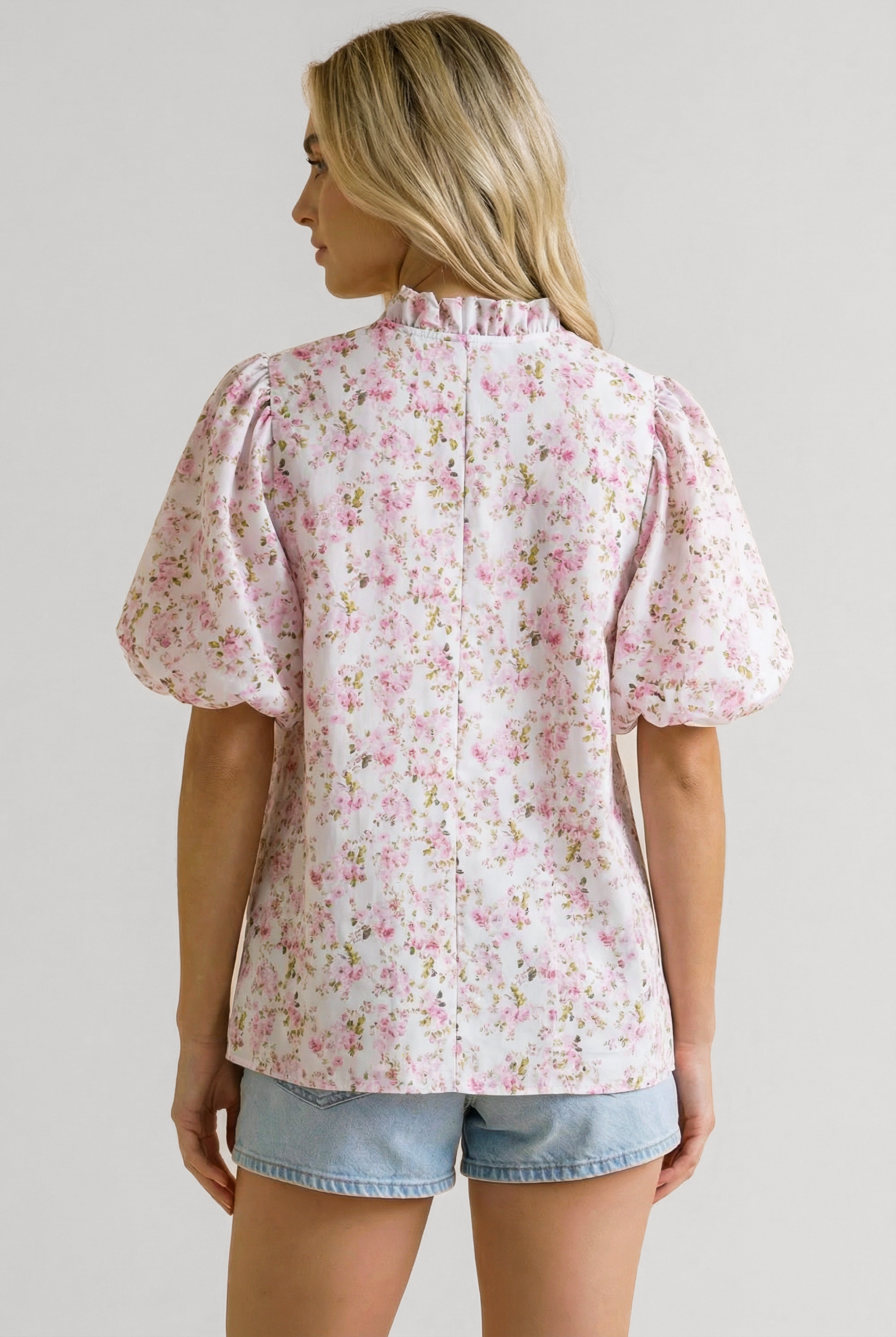 Woman wearing a pink floral blouse with puffed short sleeves and a ruffled neckline seen from the back