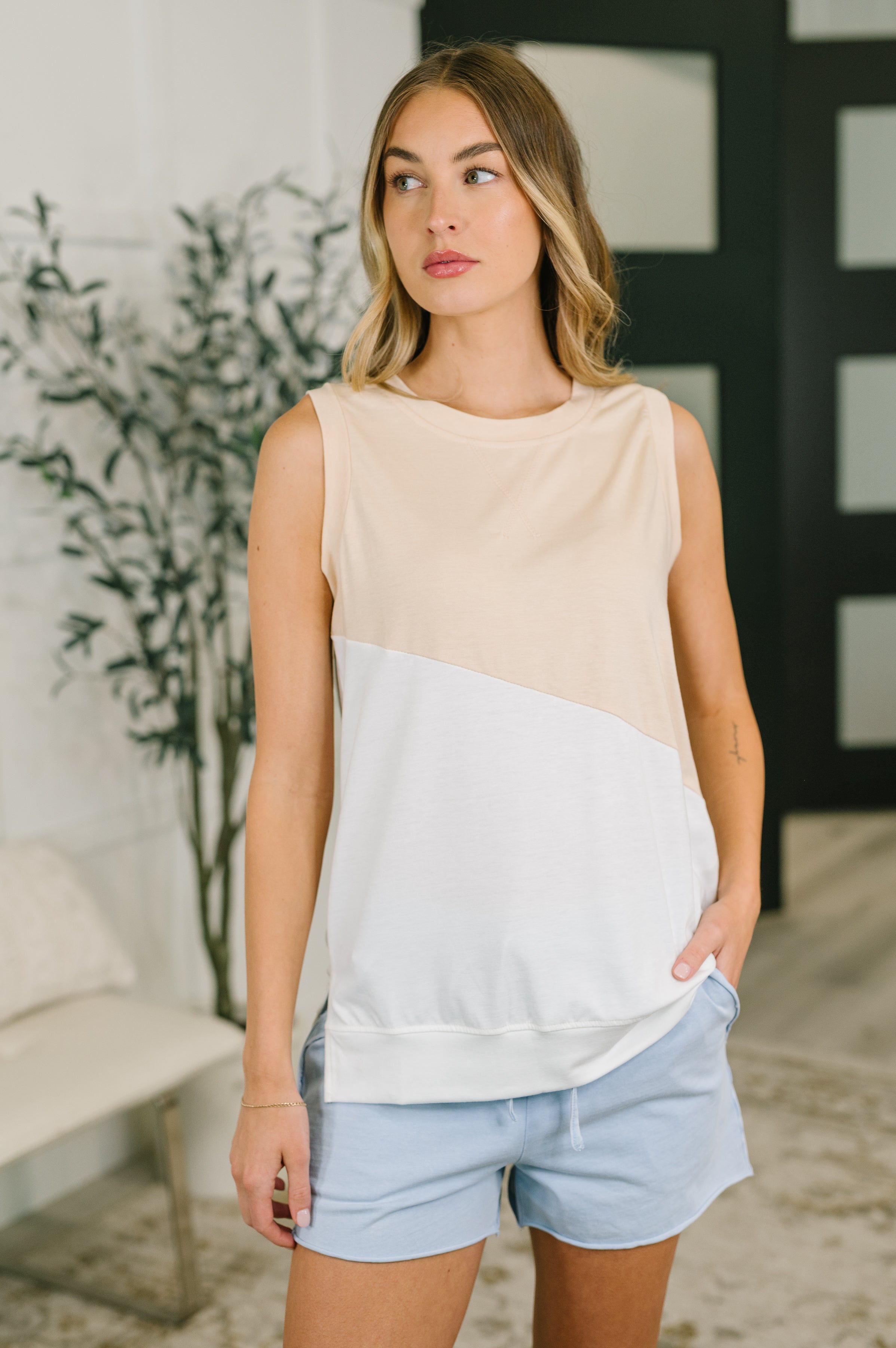 Woman wearing cream color block sleeveless top paired with light blue casual shorts indoors with neutral decor