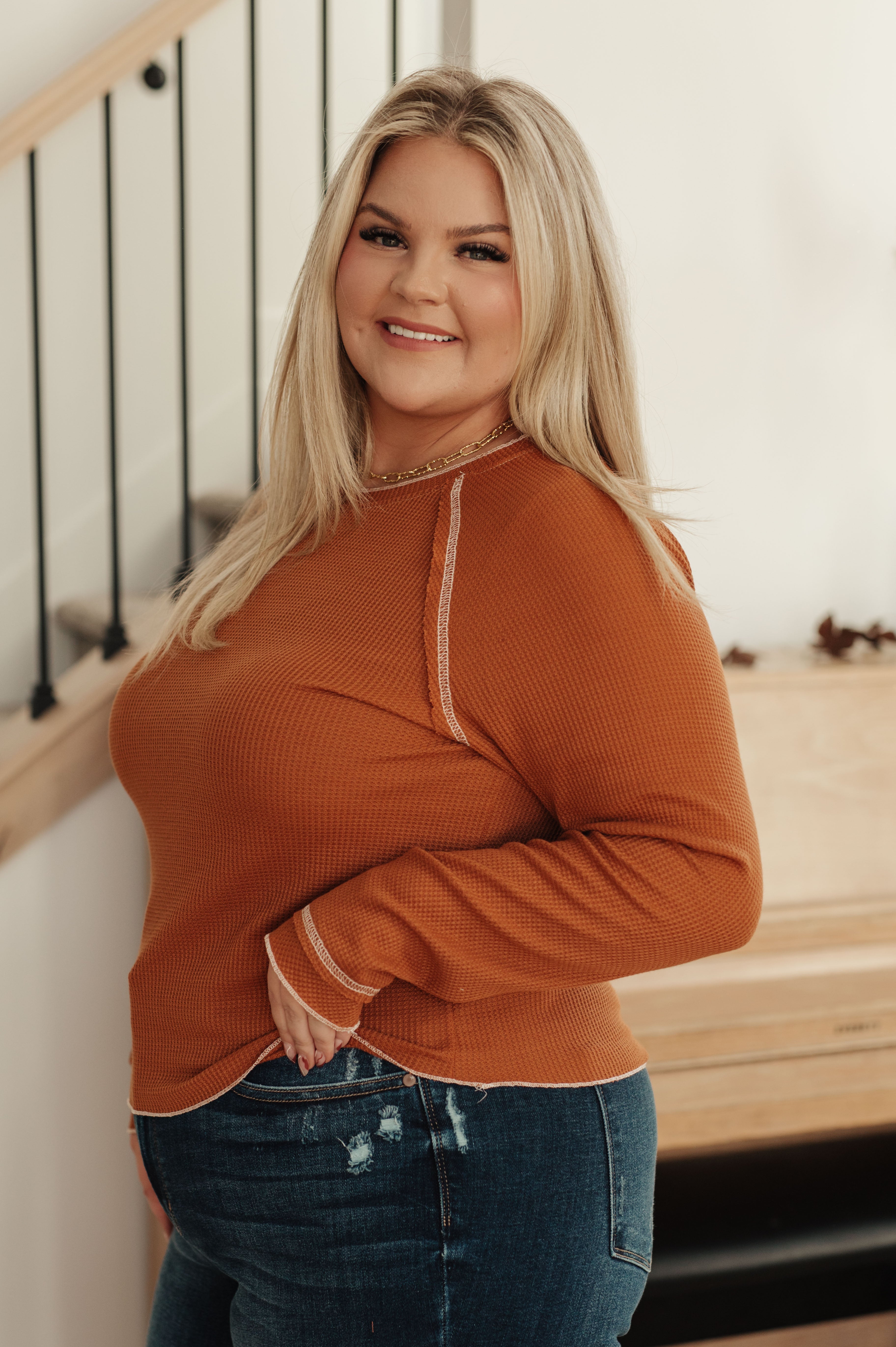 Plus-size woman smiling indoors wearing rust-colored waffle knit top with long sleeves and contrast stitching