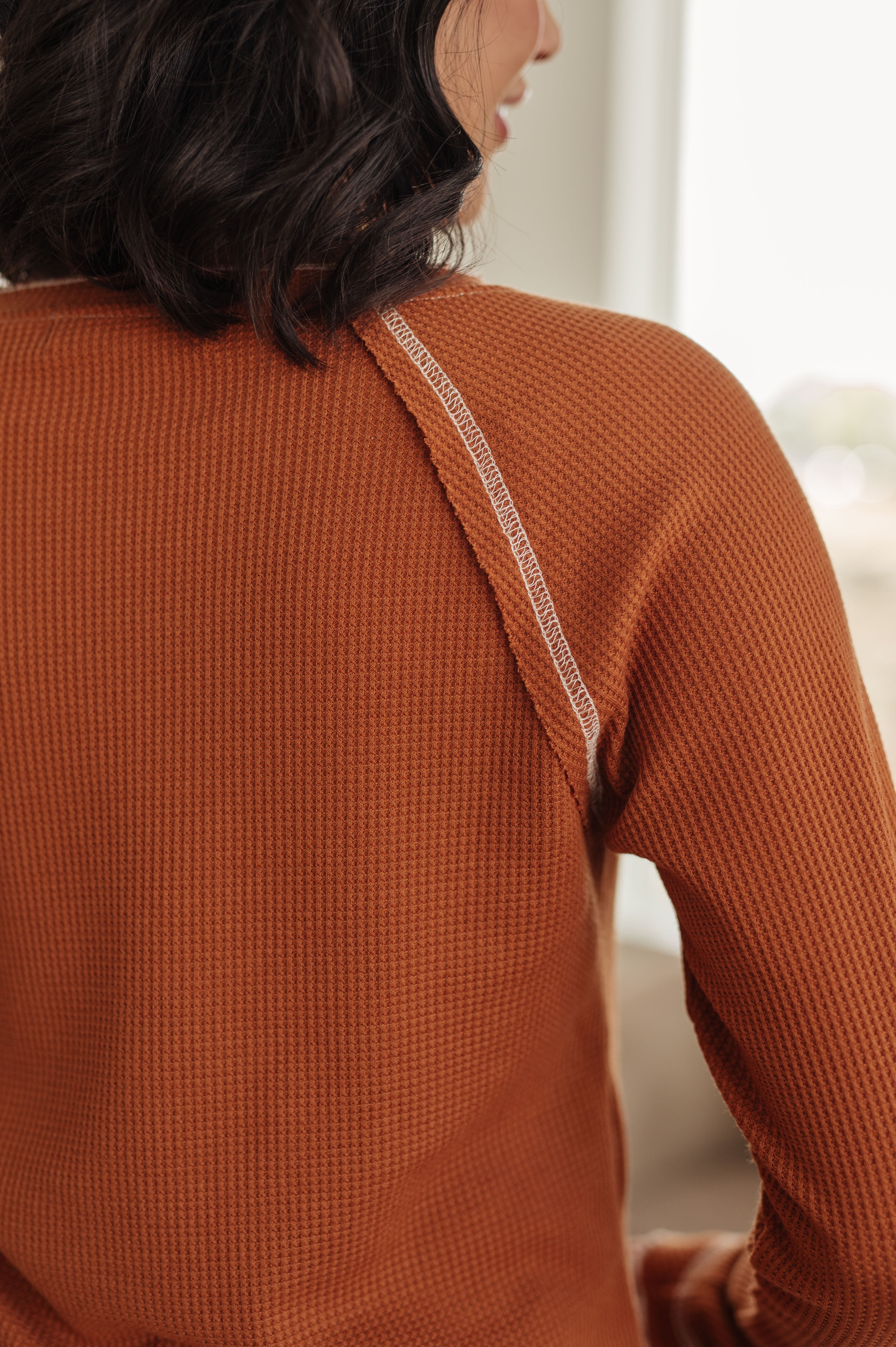 Close-up of rust-colored waffle knit top showing textured fabric and shoulder seam detail on model indoors