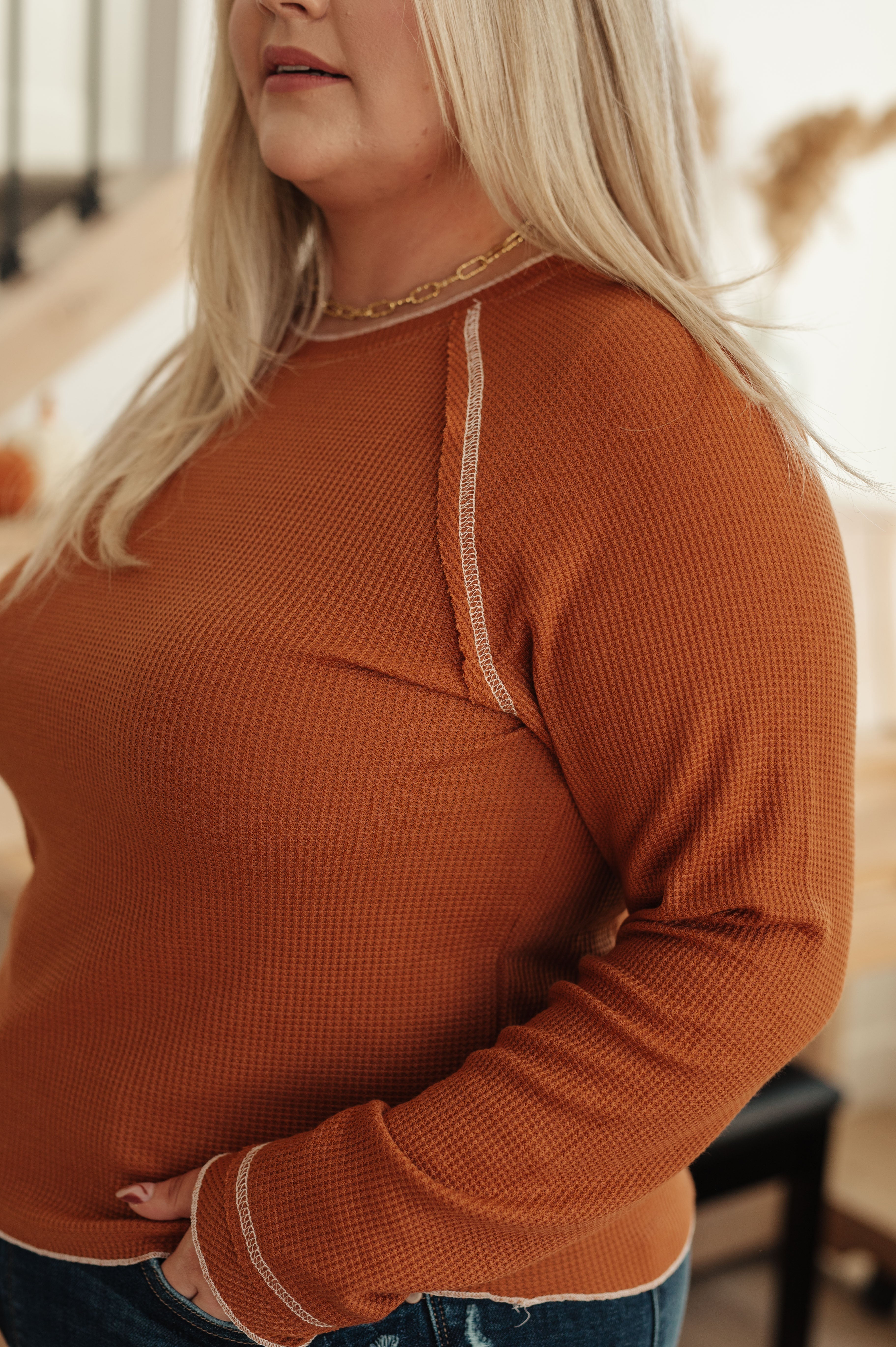 Plus-size woman wearing rust waffle knit top with long sleeves and contrast stitching in cozy indoor setting