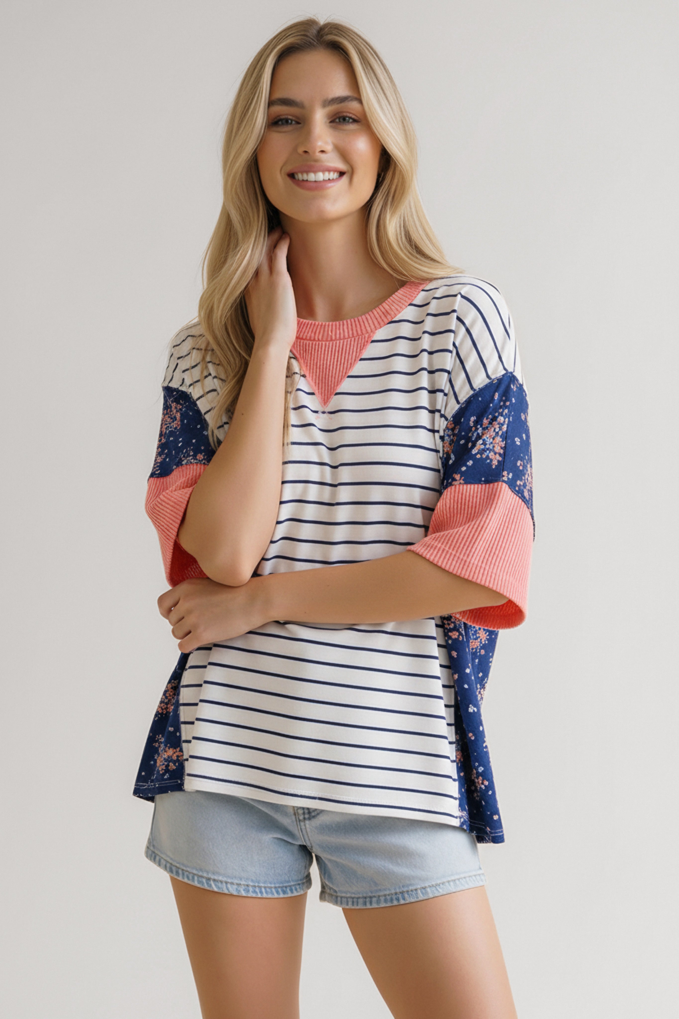 Smiling woman wearing blue striped and floral mixed media top with coral textured accents and light denim shorts