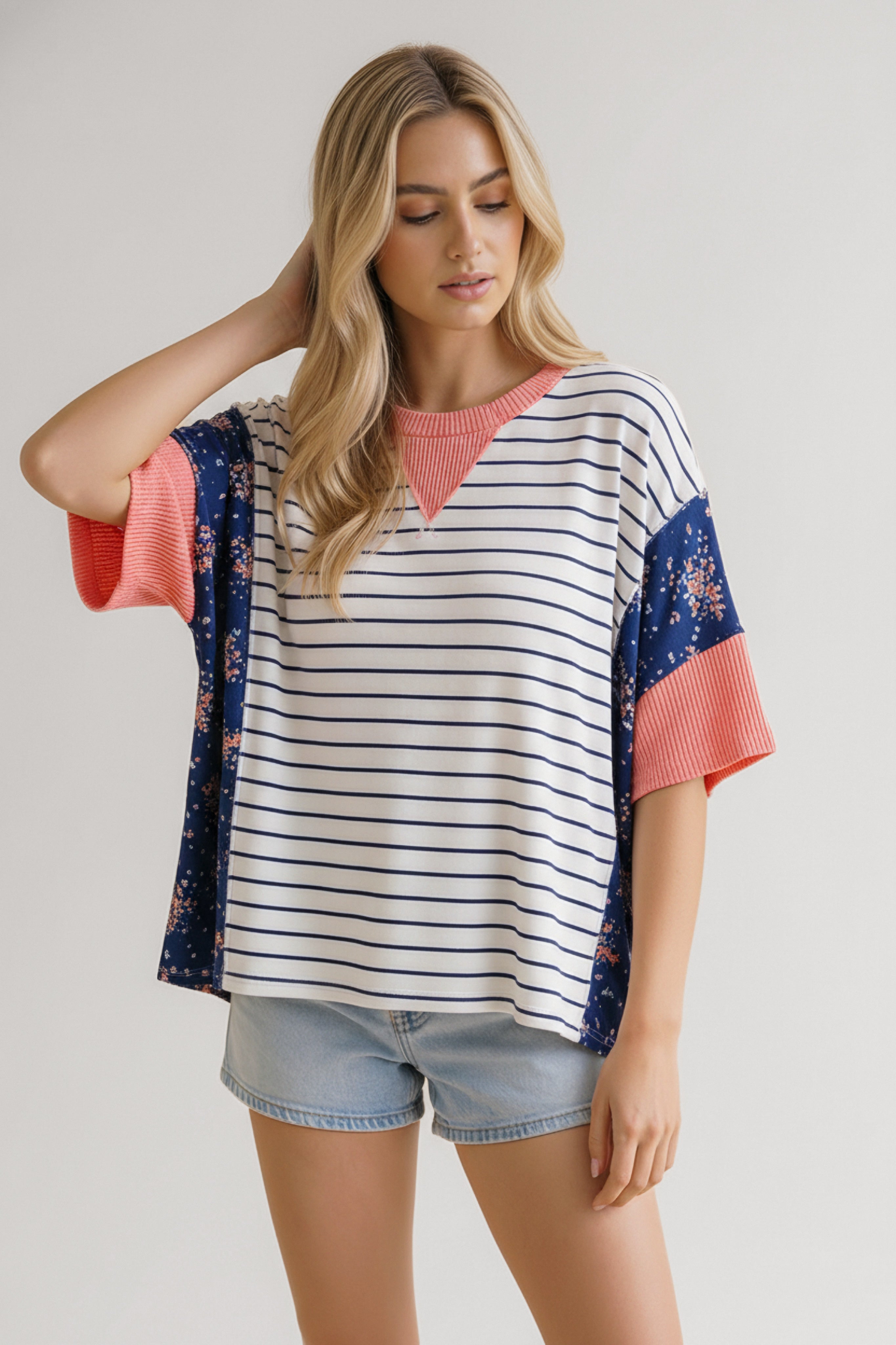 Woman wearing loose blue striped and floral mixed media top with coral ribbed neckline and sleeves paired with denim shorts