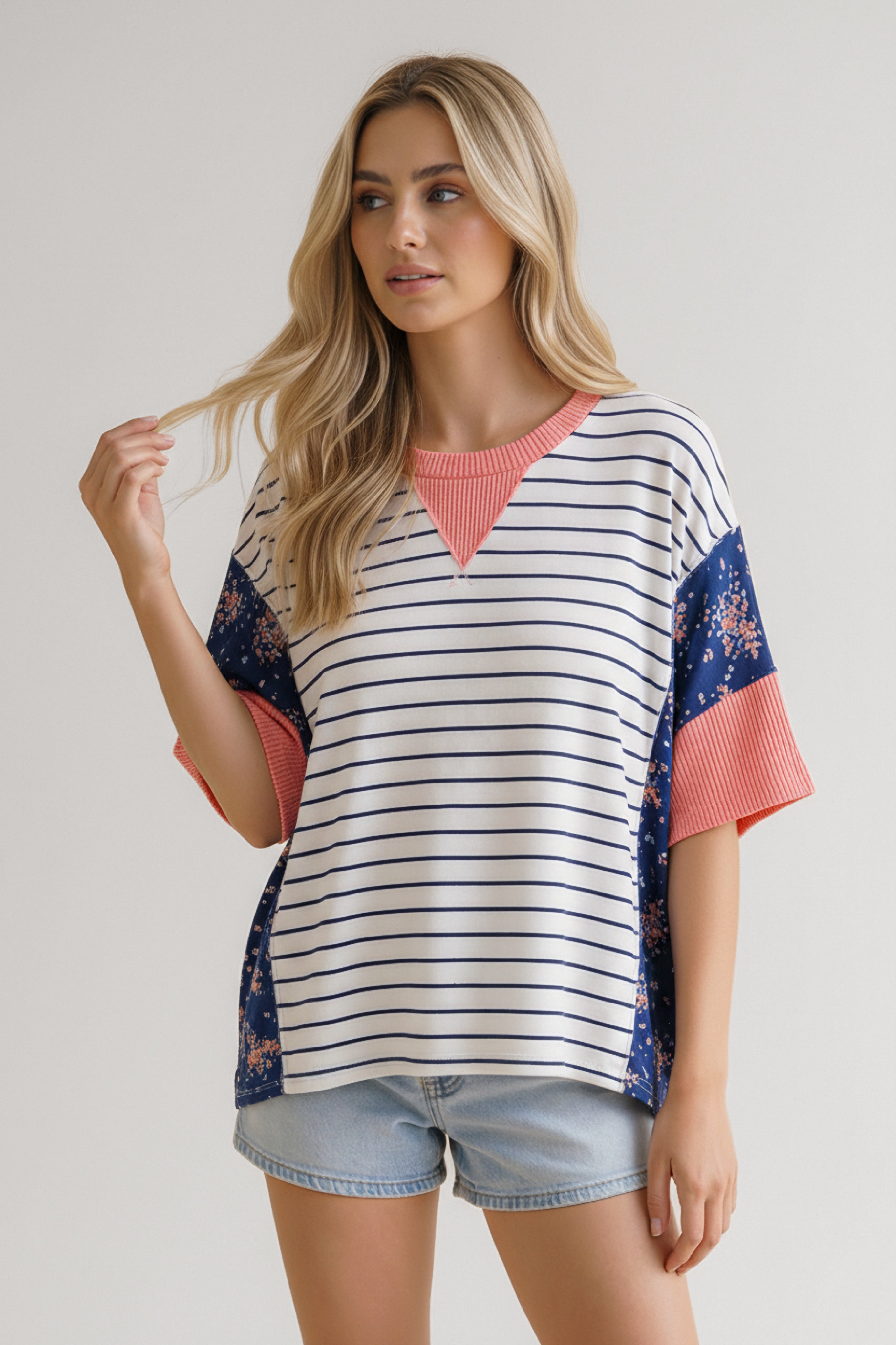Woman wearing blue and white striped mixed media top with floral panels and coral ribbed neckline and sleeves paired with denim shorts