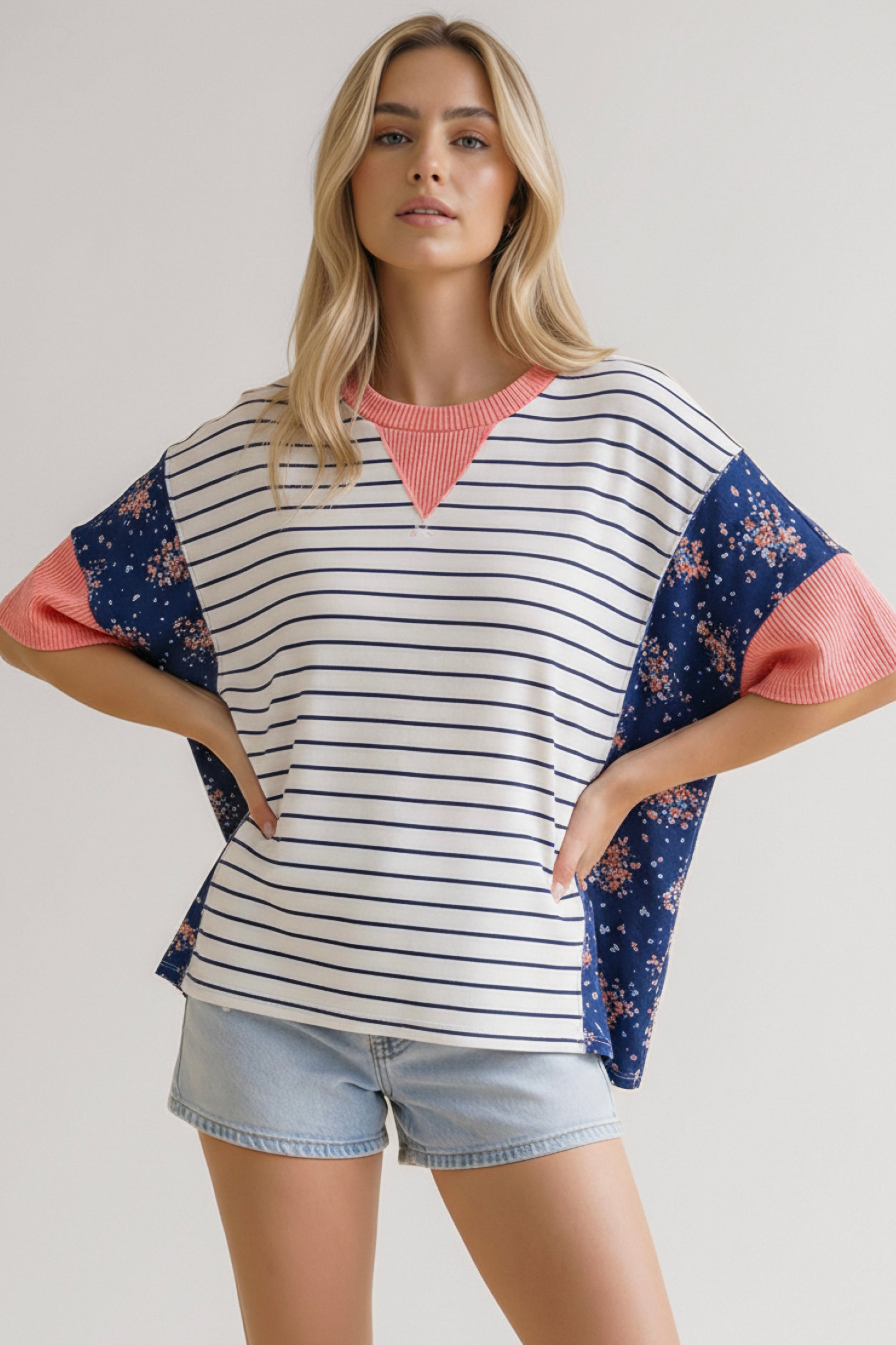Woman wearing blue striped and floral mixed media top with coral ribbed neckline and sleeves paired with light denim shorts