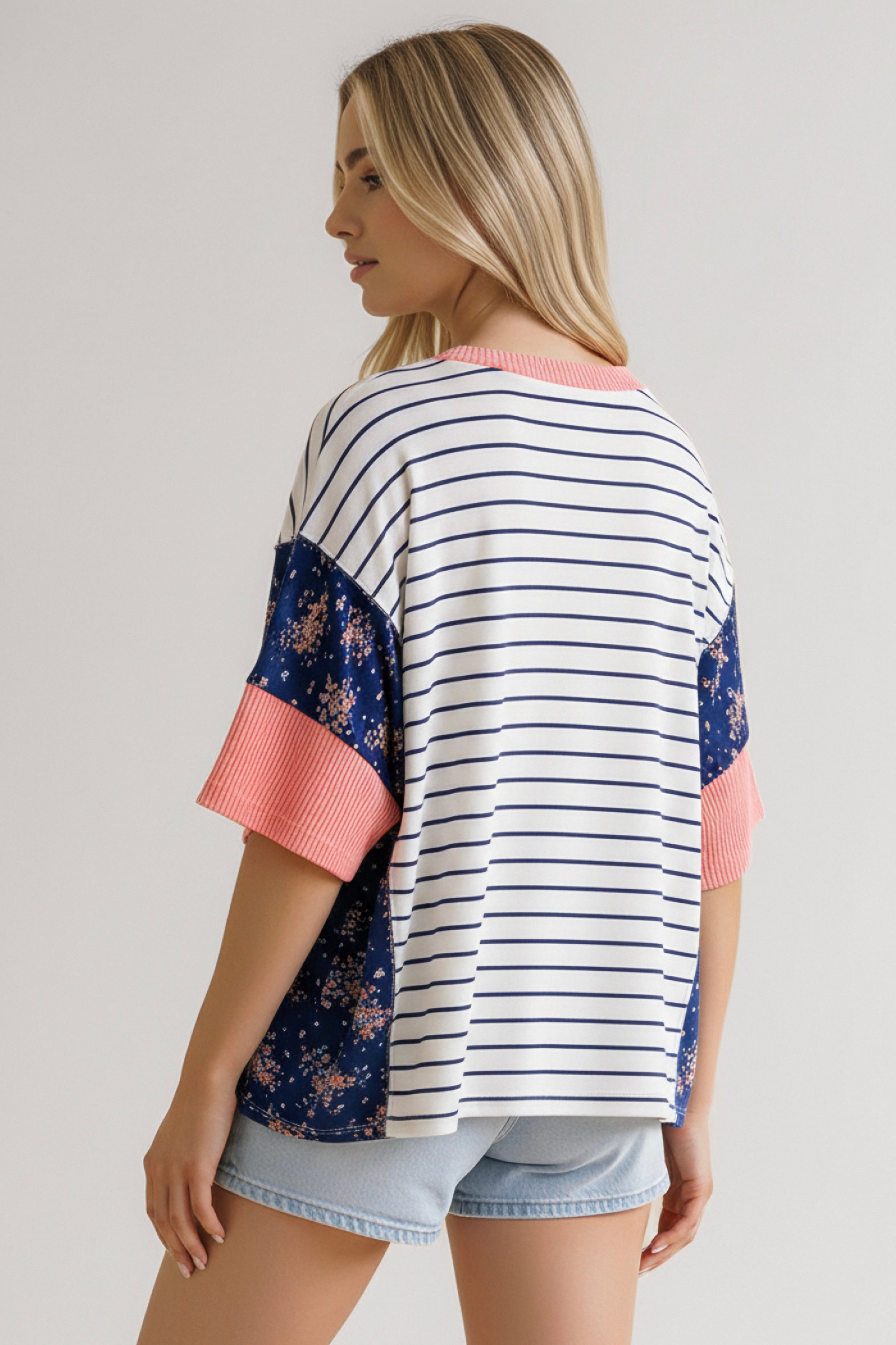 Woman wearing blue striped and floral top with coral ribbed cuffs paired with light denim shorts viewed from back