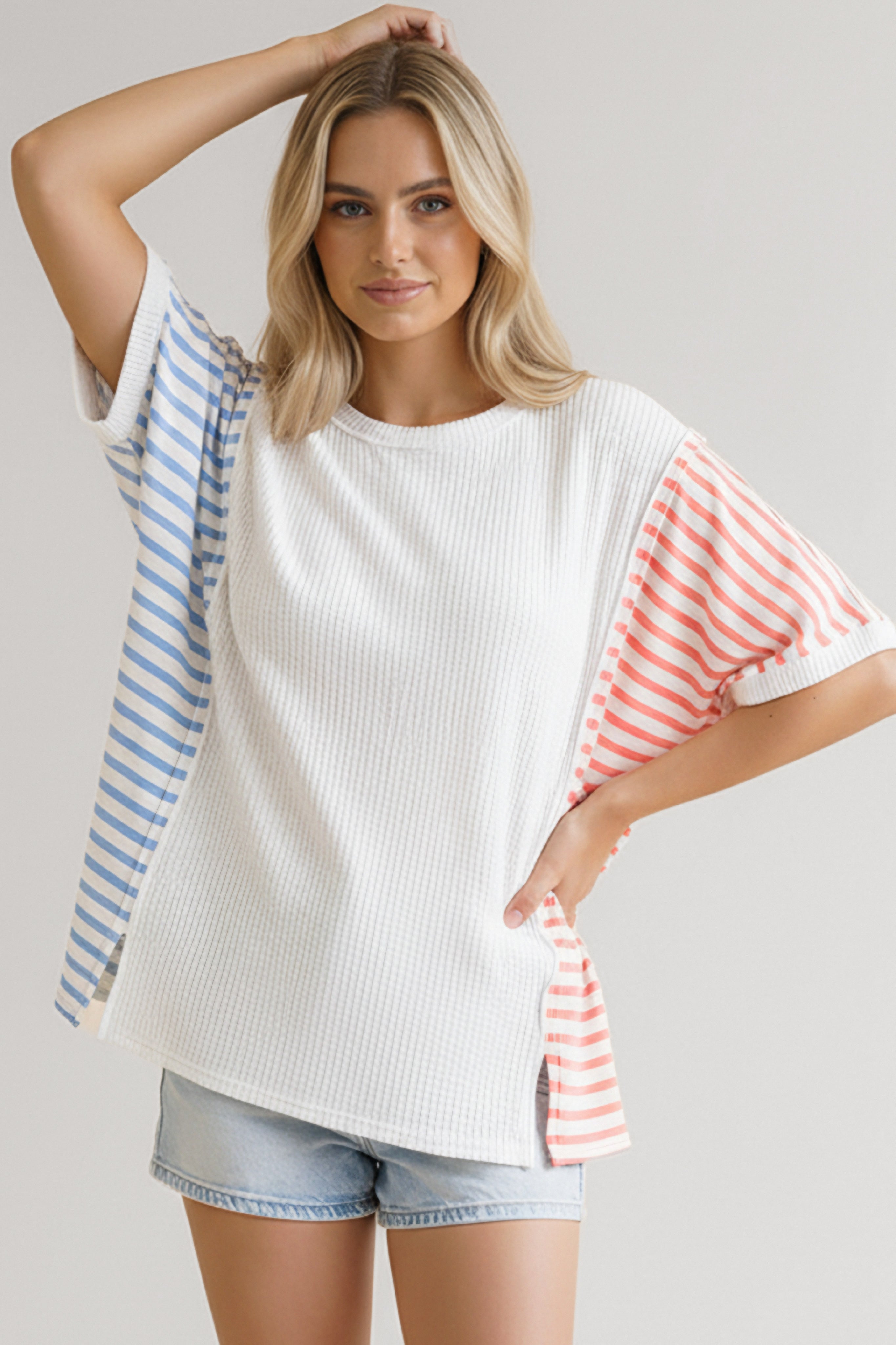 Woman wearing ivory waffle knit top with blue and coral striped sleeves paired with light denim shorts