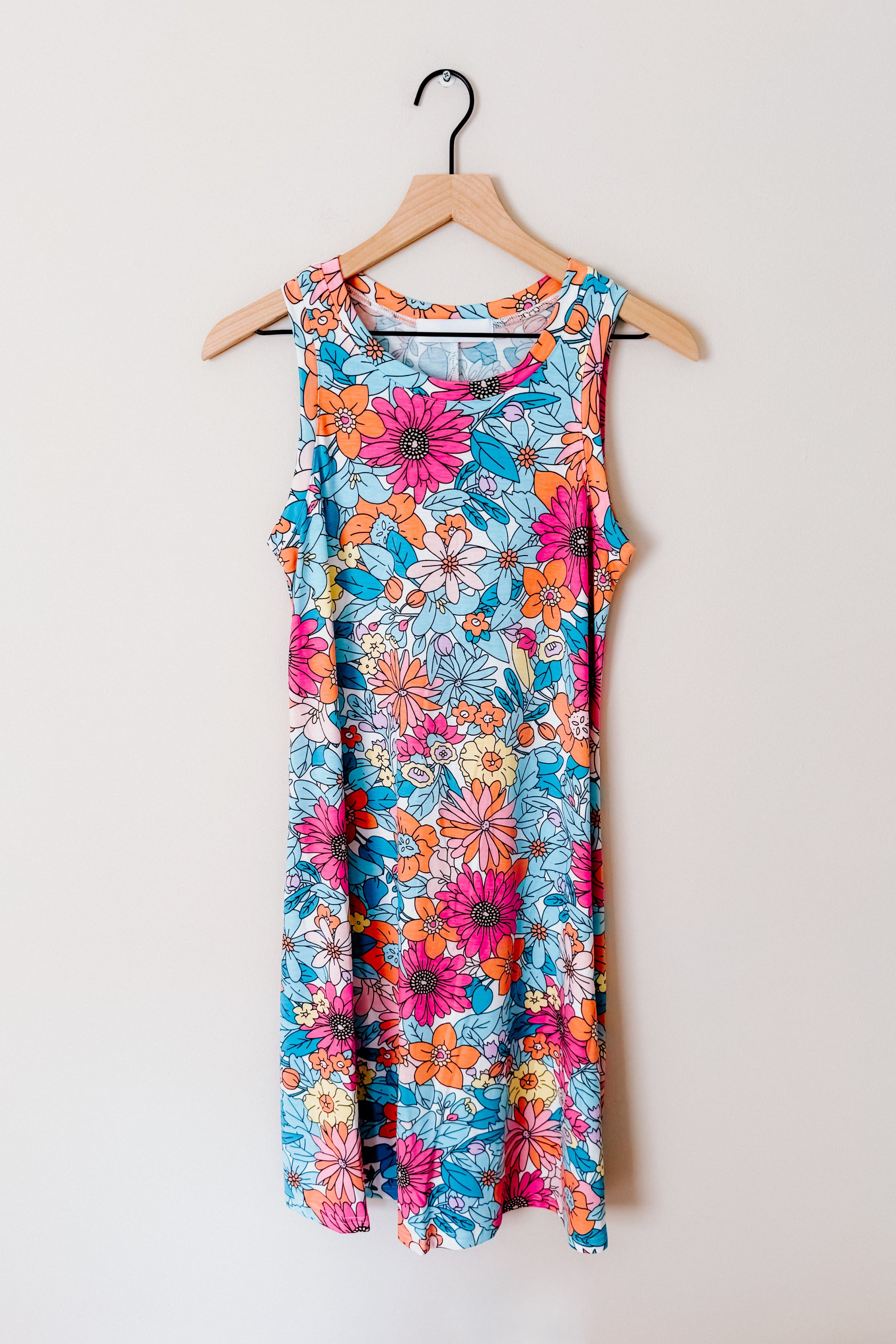 Sleeveless swing dress with vibrant floral print in blue, pink, and orange tones hanging on wooden hanger