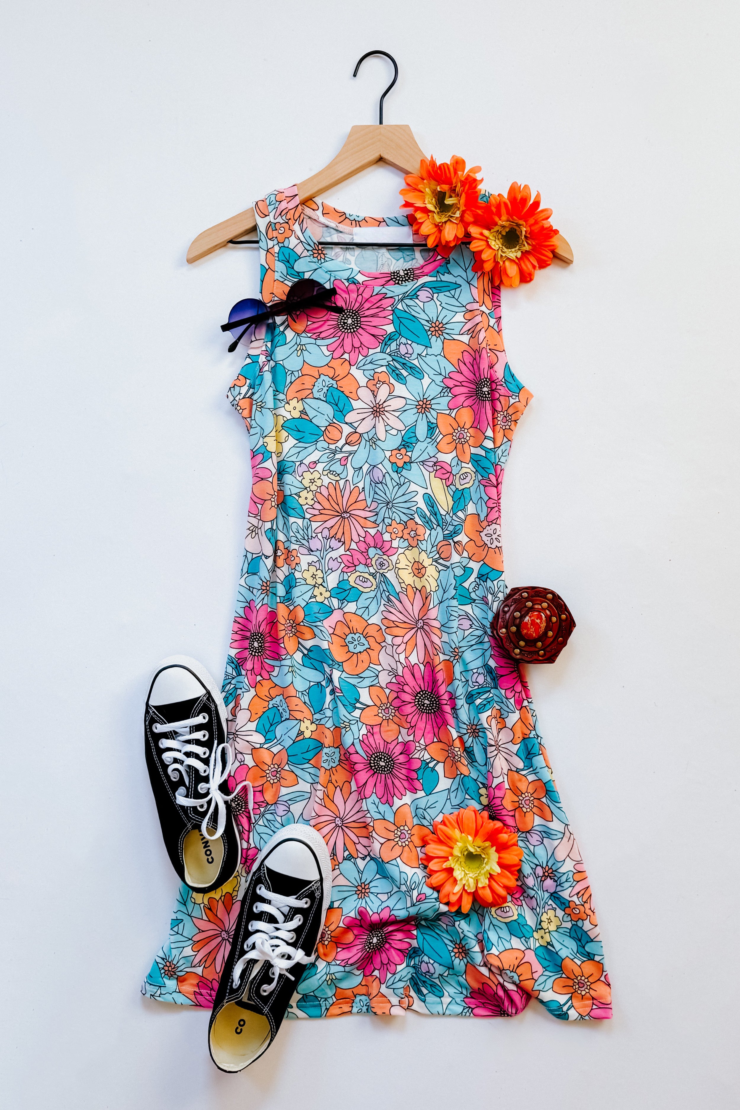 Blue floral sleeveless swing dress paired with black sneakers and decorated with orange flowers and sunglasses