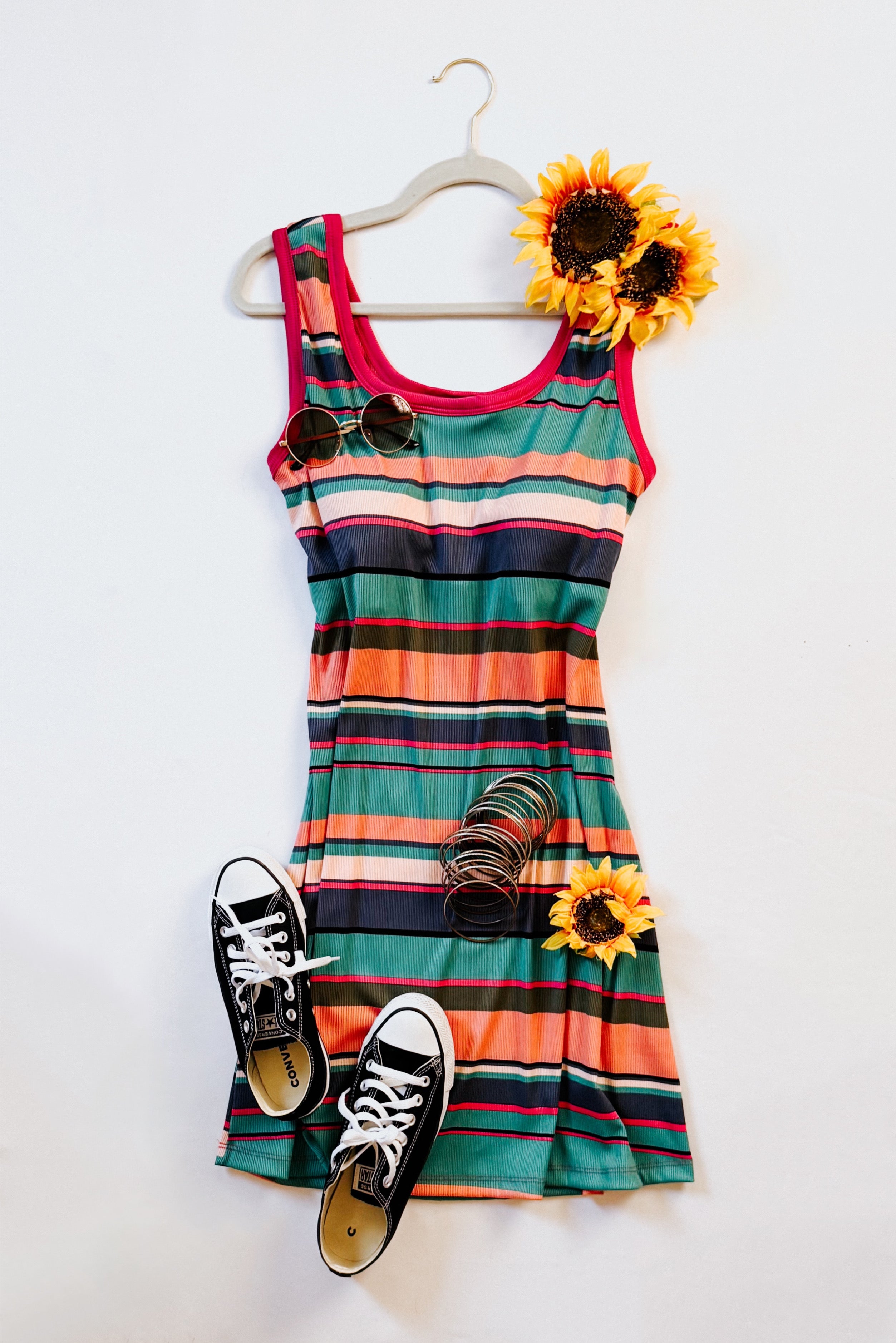Striped tank dress with bold red trim styled with black sneakers, sunglasses, bracelets, and sunflower accents on hanger