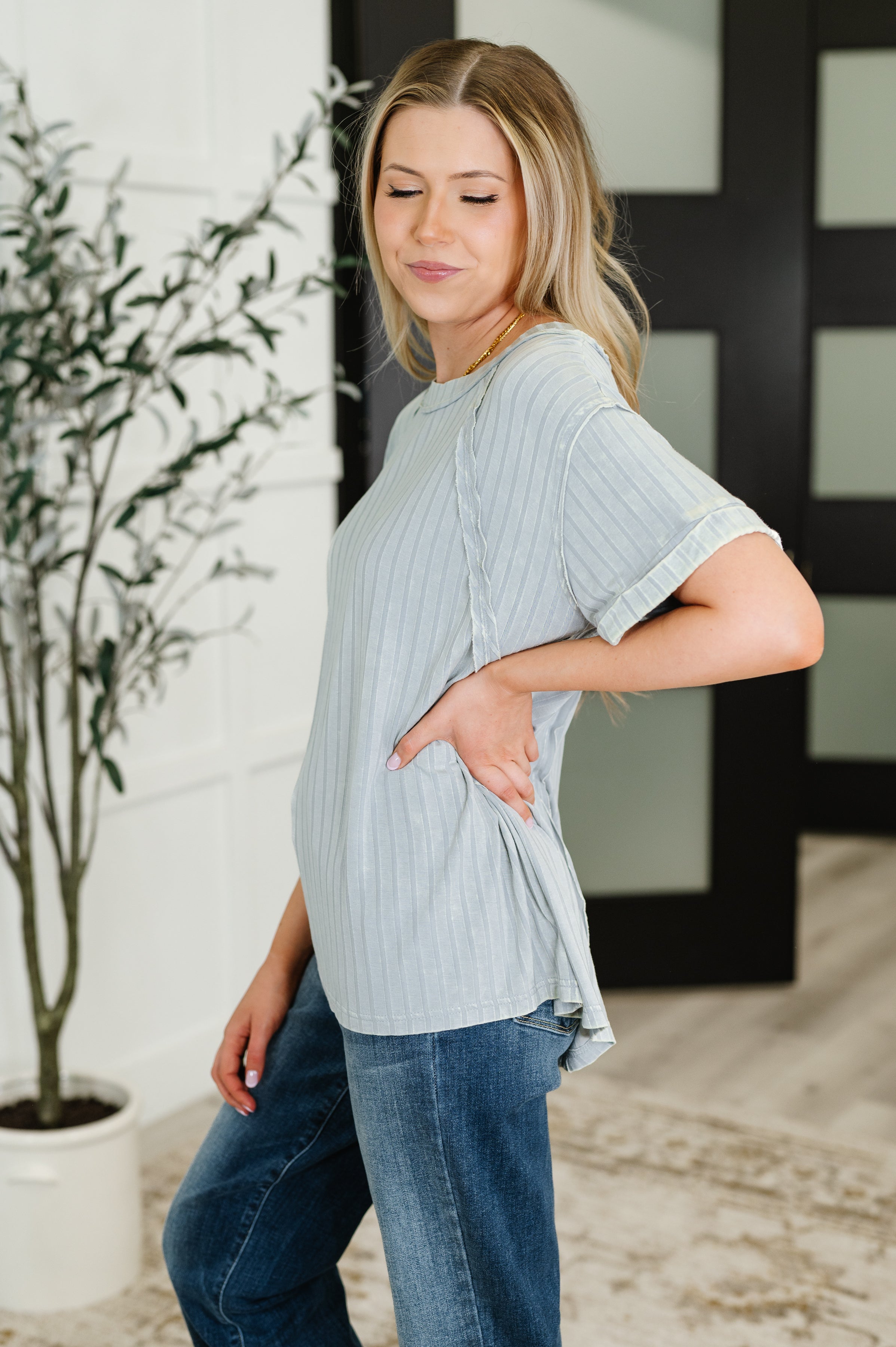 Woman wearing light grey mineral wash ribbed top with rolled sleeves paired with medium wash jeans indoors