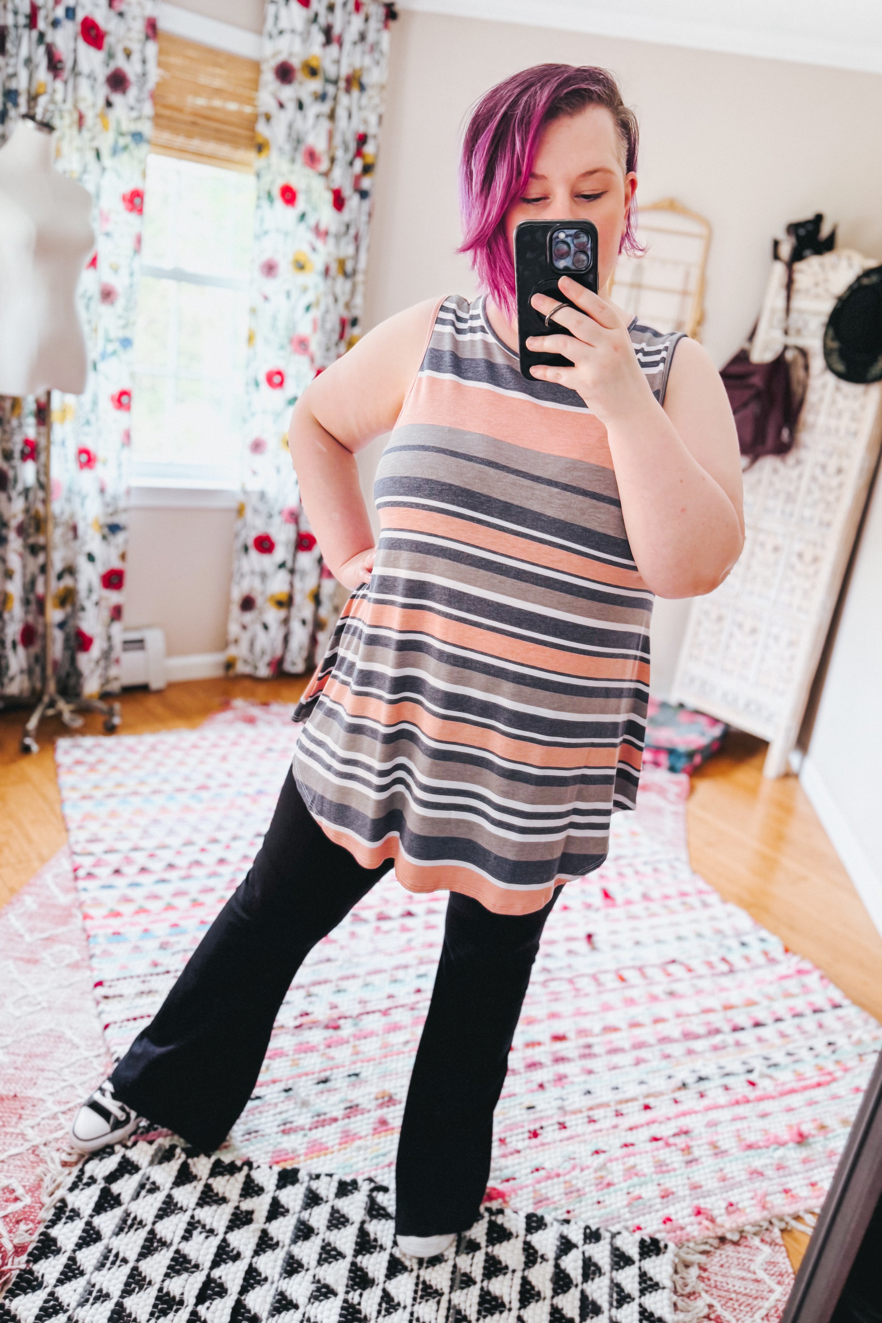 Woman with pink hair wearing a sleeveless striped top in soft pink and gray tones paired with black pants indoors
