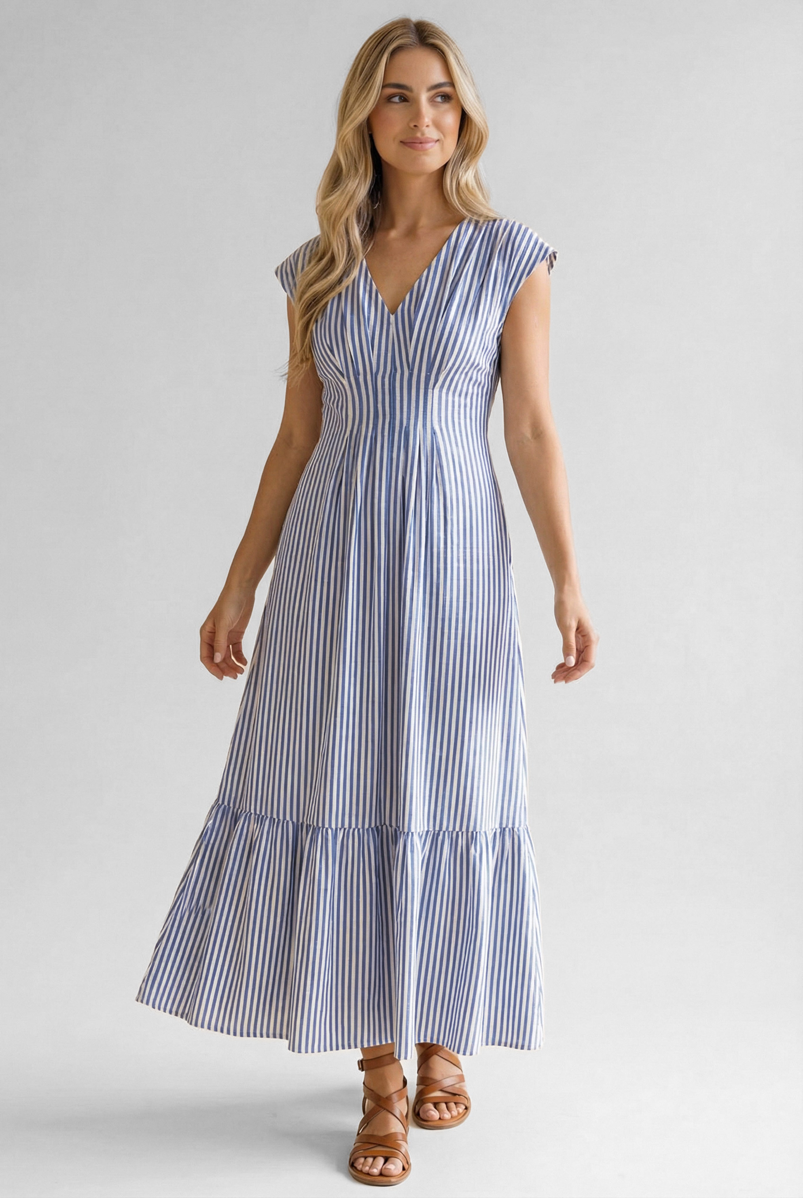 Woman wearing blue striped midi dress with cap sleeves and tiered hem paired with brown strappy sandals indoors