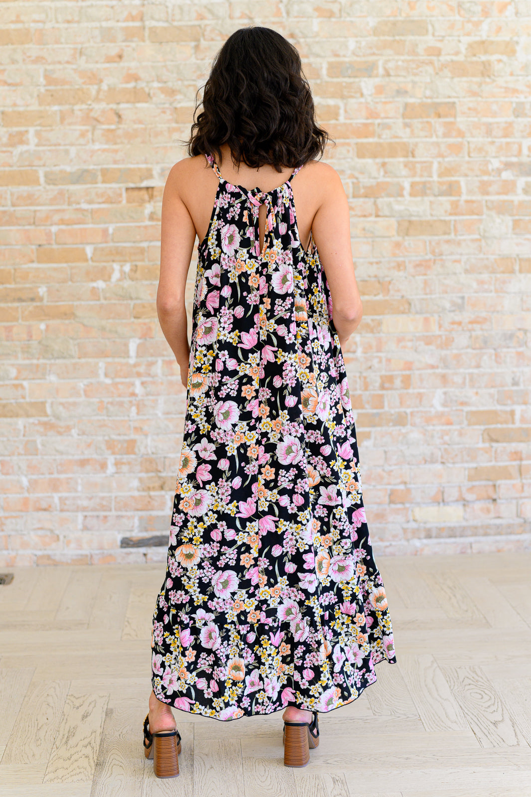 Back view of a woman wearing a black dress with pink and yellow floral print and thin shoulder straps indoors