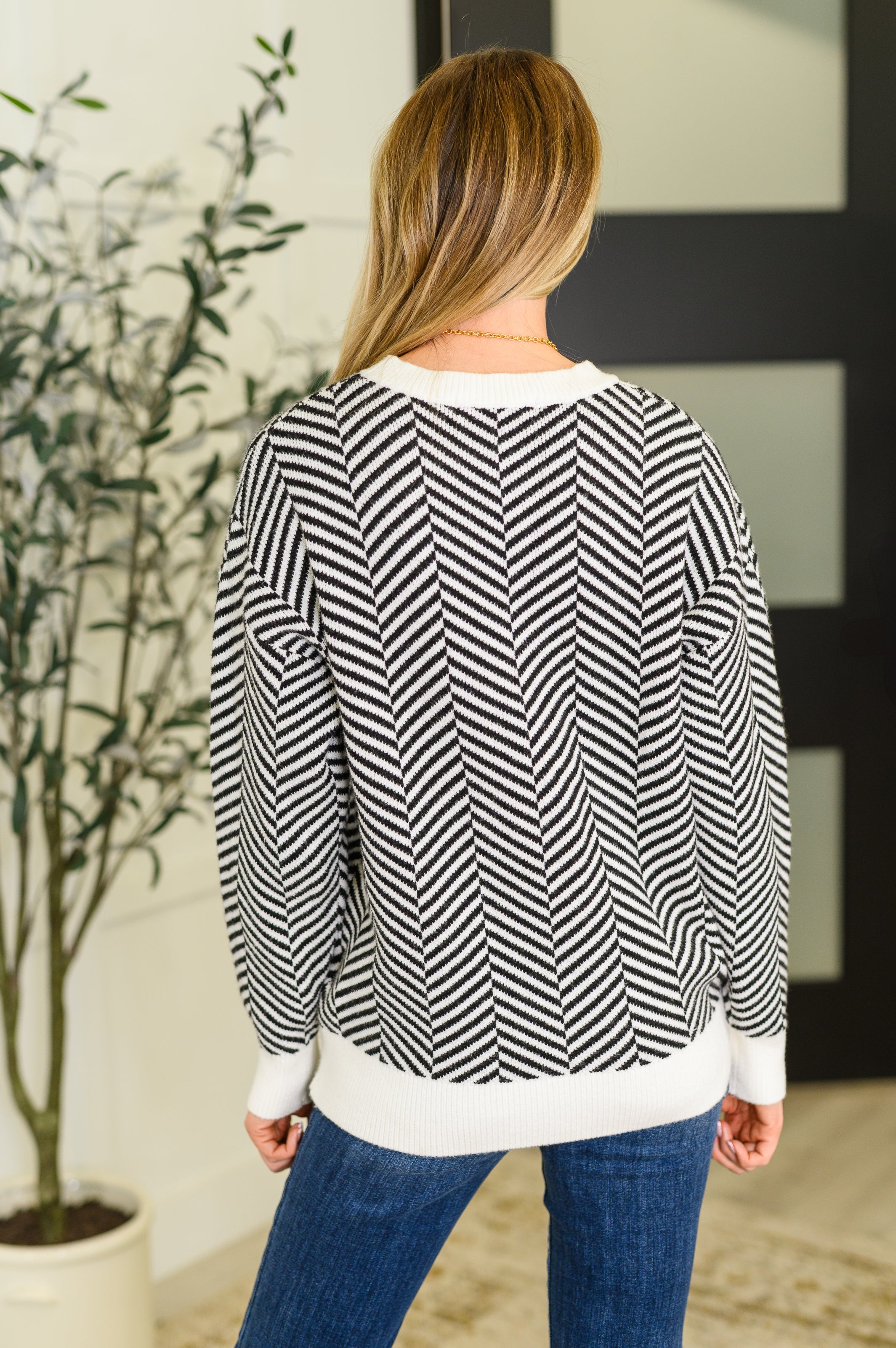 Woman wearing a black and white chevron patterned sweater with white cuffs and hem, standing indoors near a plant
