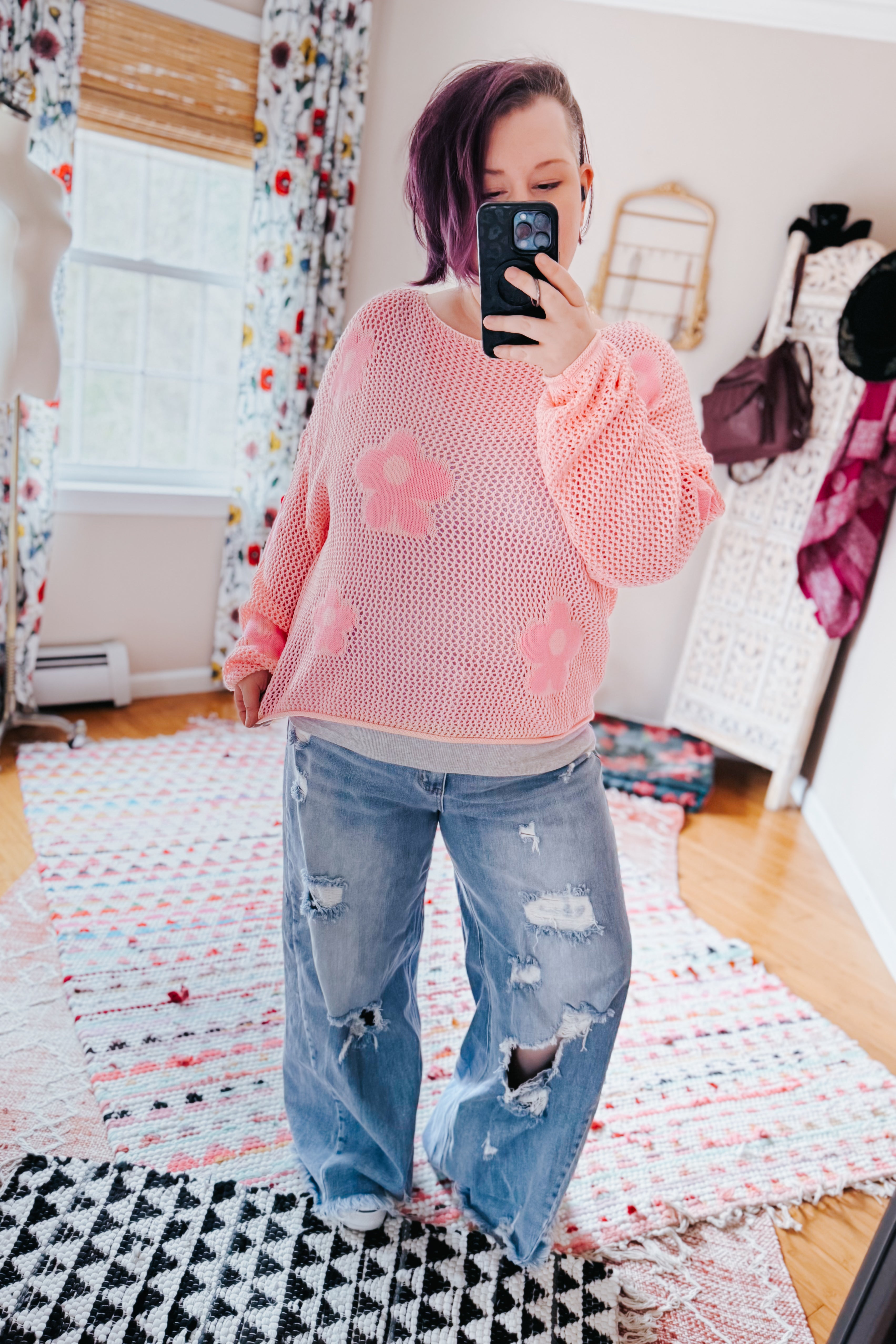 Woman wearing a blush pink floral mesh sweater top with oversized sleeves paired with distressed wide-leg jeans indoors