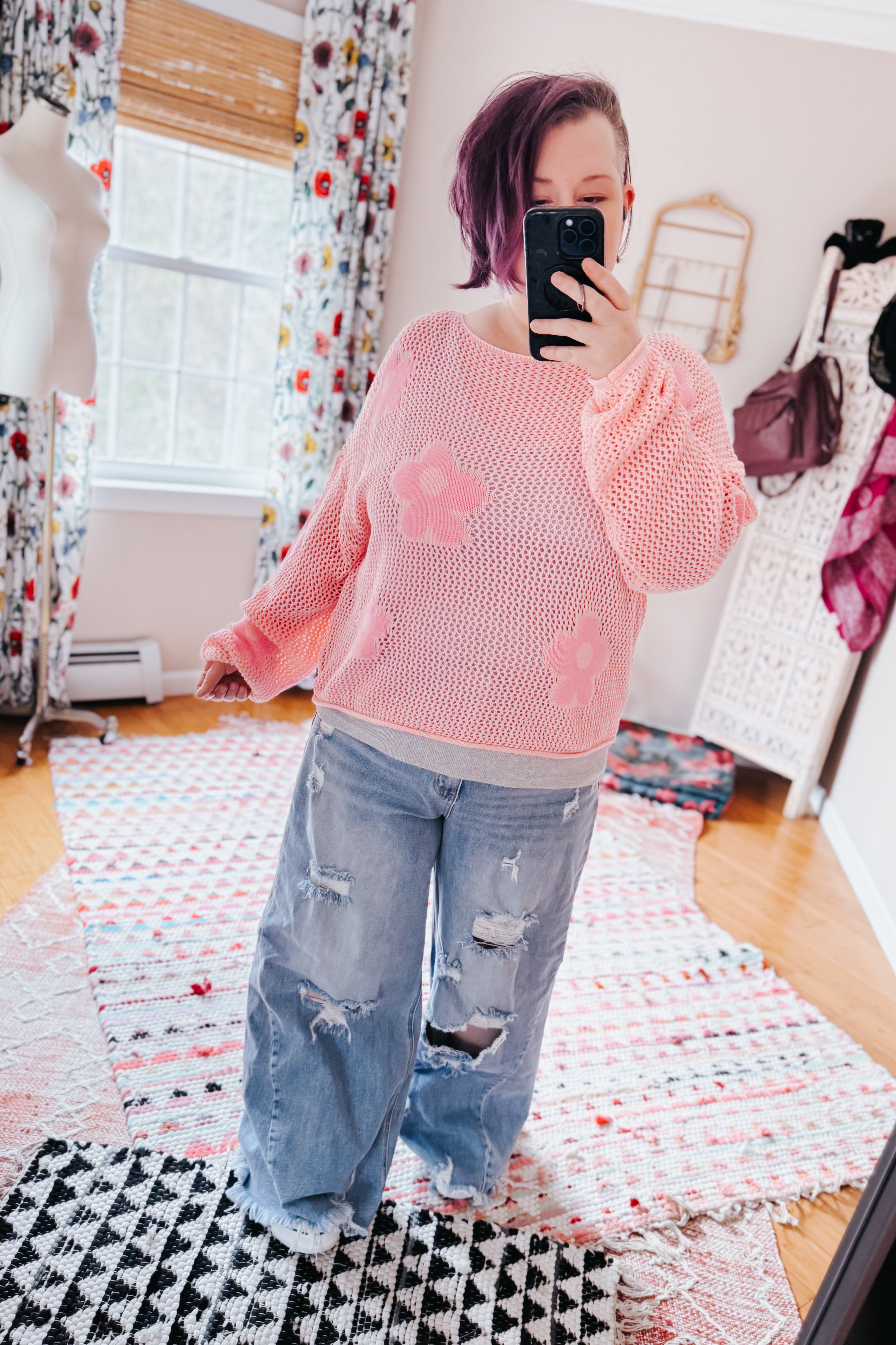 Woman wearing a blush pink floral mesh sweater with wide sleeves paired with distressed wide-leg jeans indoors