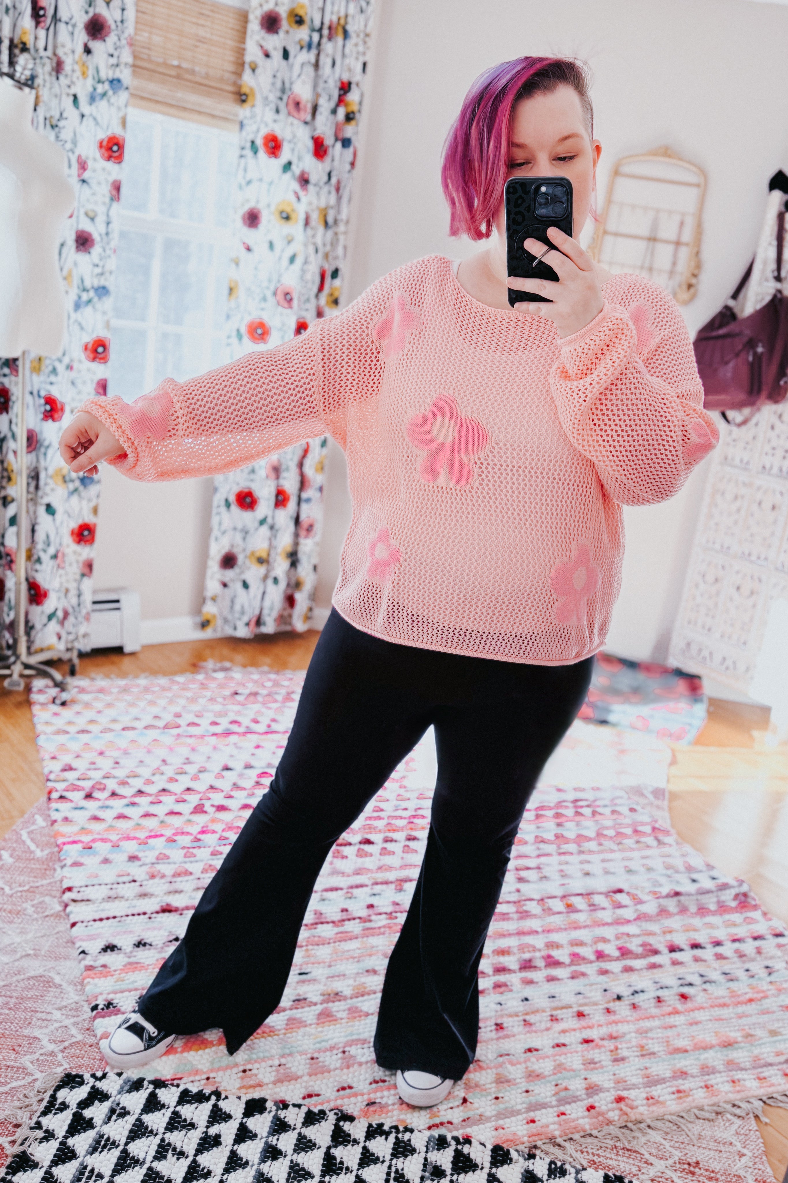 Woman wearing a blush pink mesh sweater top with floral accents paired with black wide-leg pants indoors taking a selfie