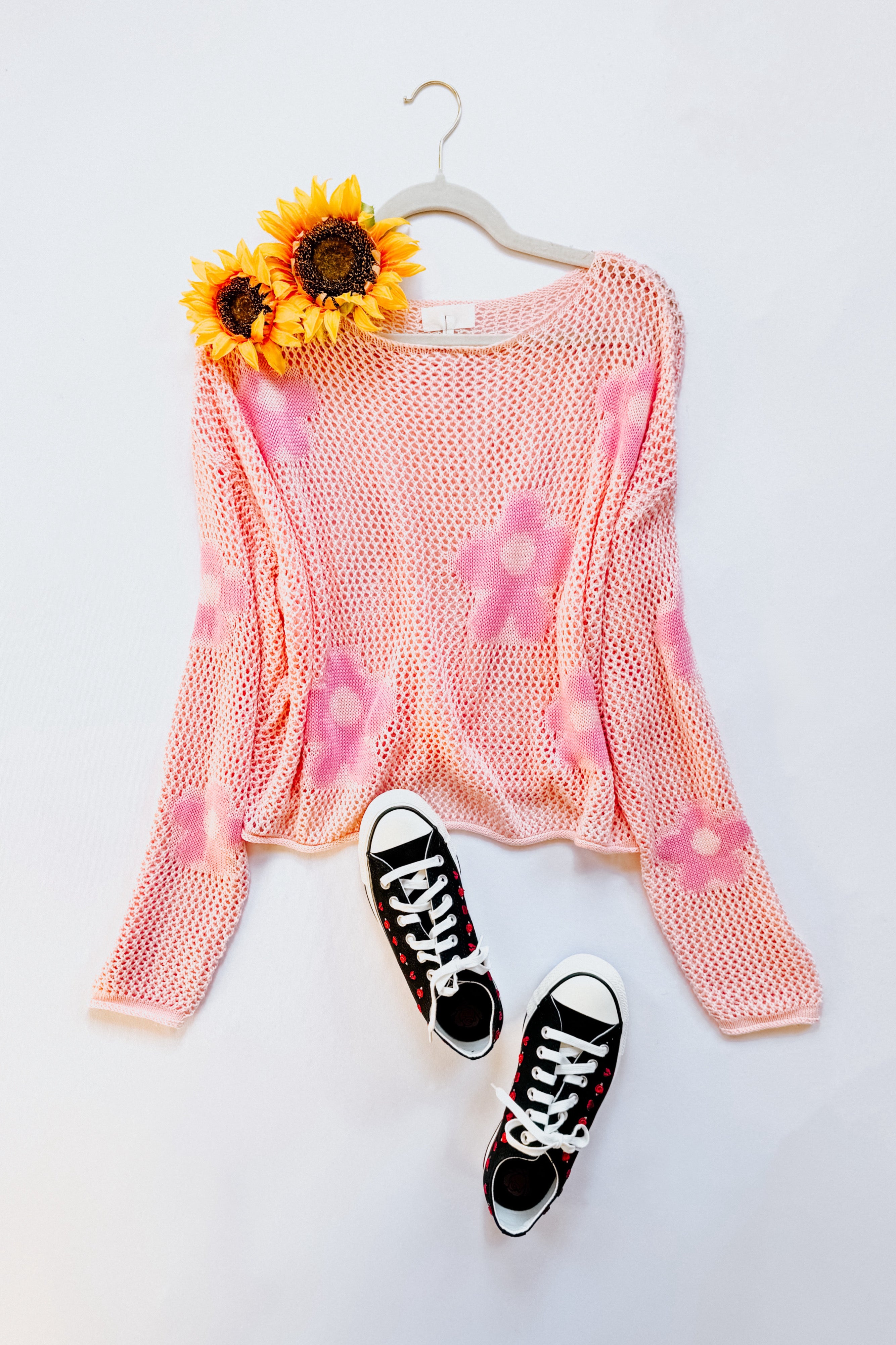 Blush pink floral mesh sweater with long sleeves on hanger paired with black and red polka dot sneakers and sunflowers