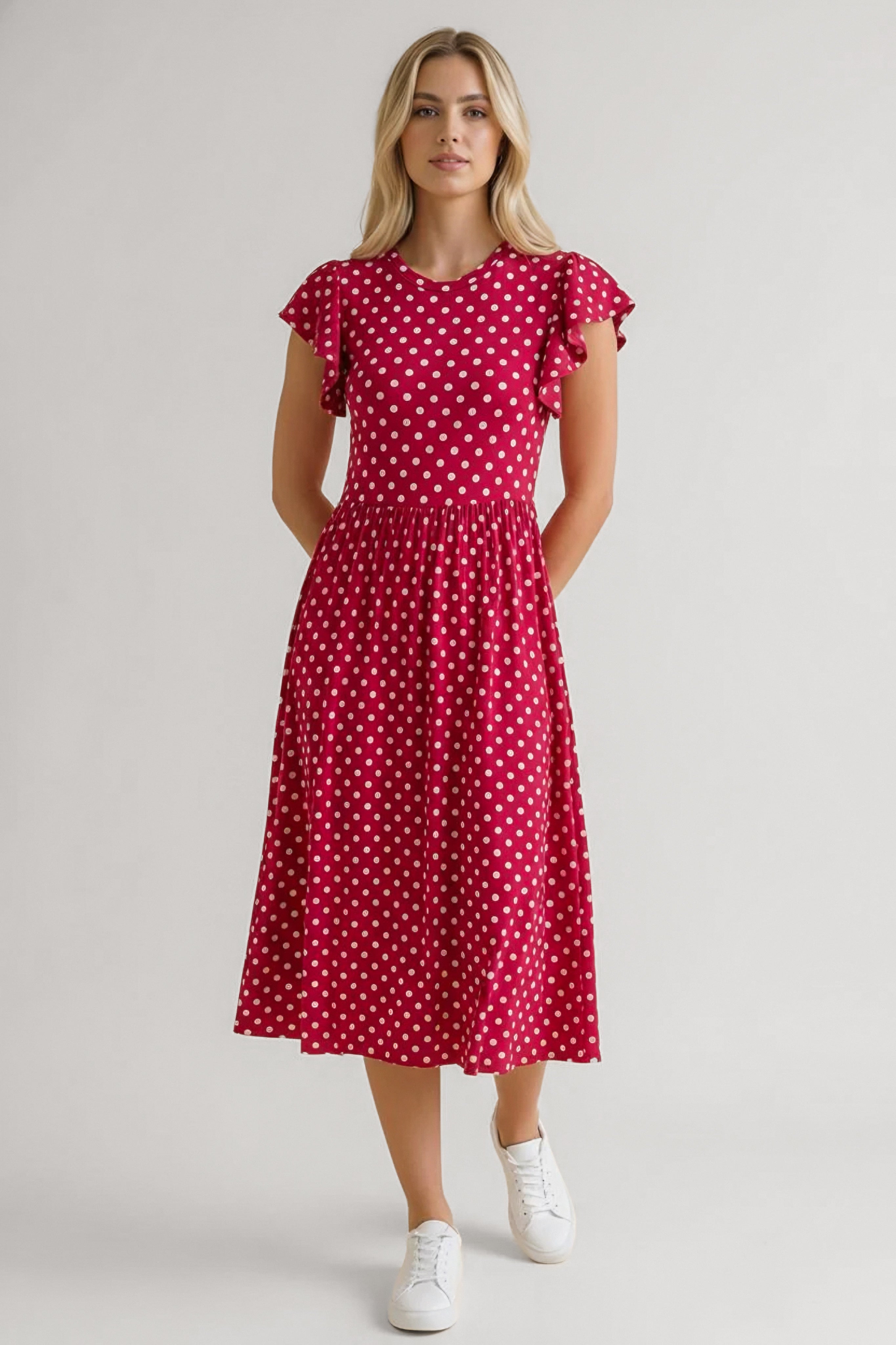Woman wearing a red polka dot midi dress with flutter sleeves paired with white sneakers in relaxed pose