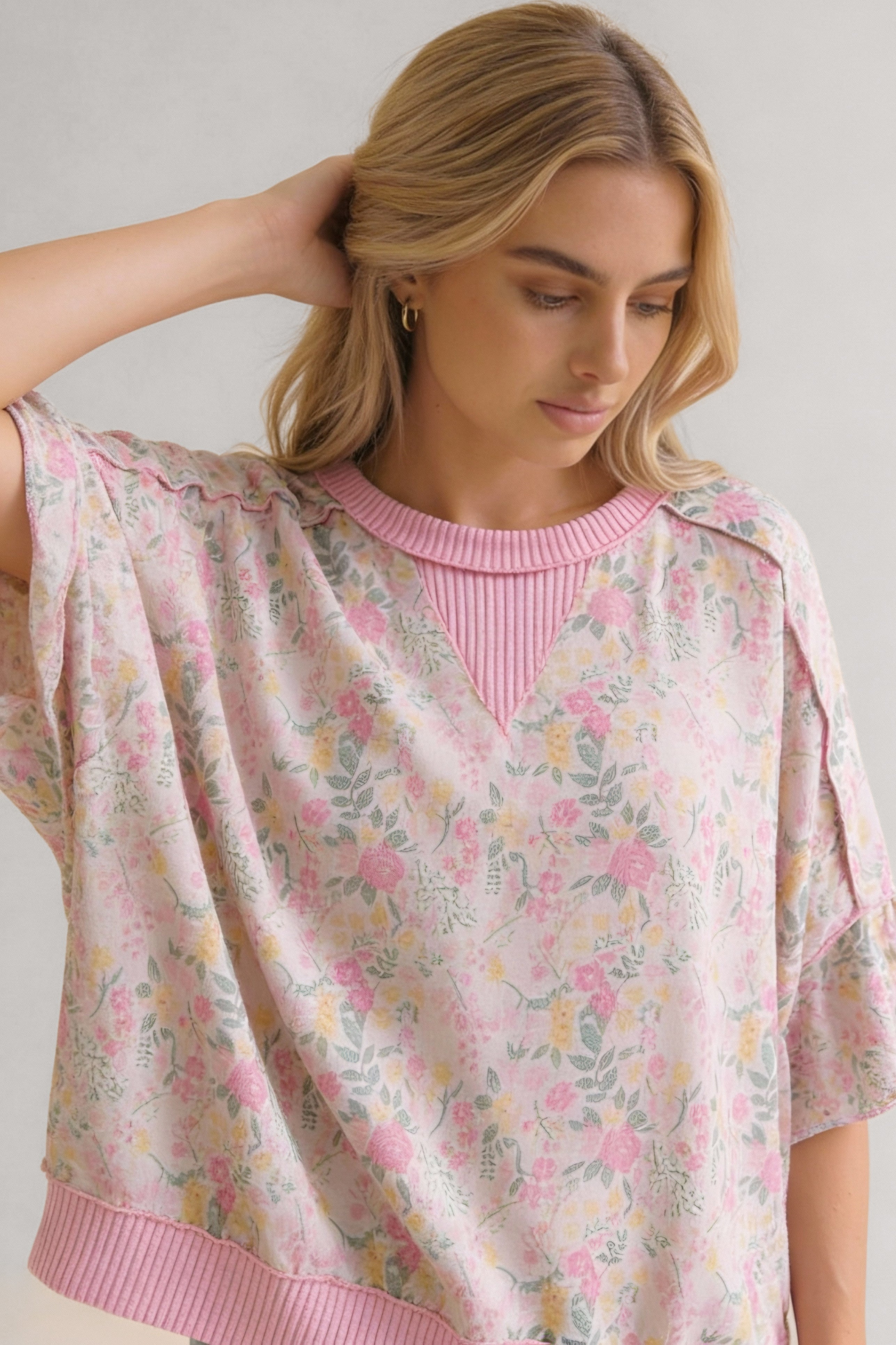 Woman wearing a loose pink sweater with a floral pattern and ribbed collar, hem, and V-neck detail