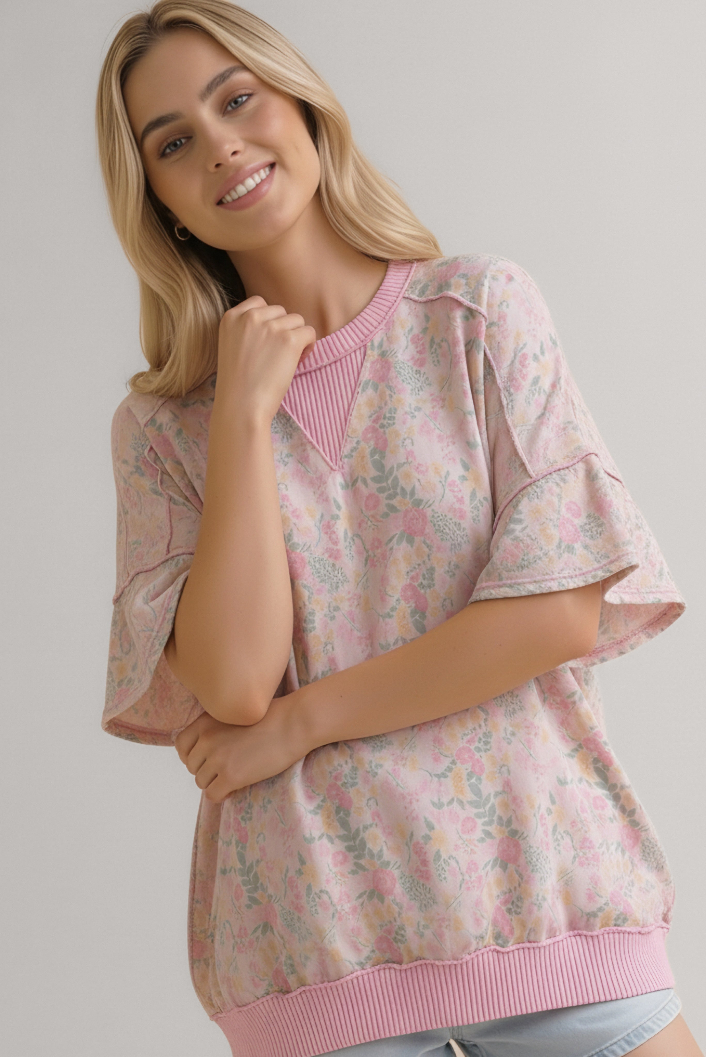Smiling woman wearing a pink floral print top with short wide sleeves and ribbed collar and hem