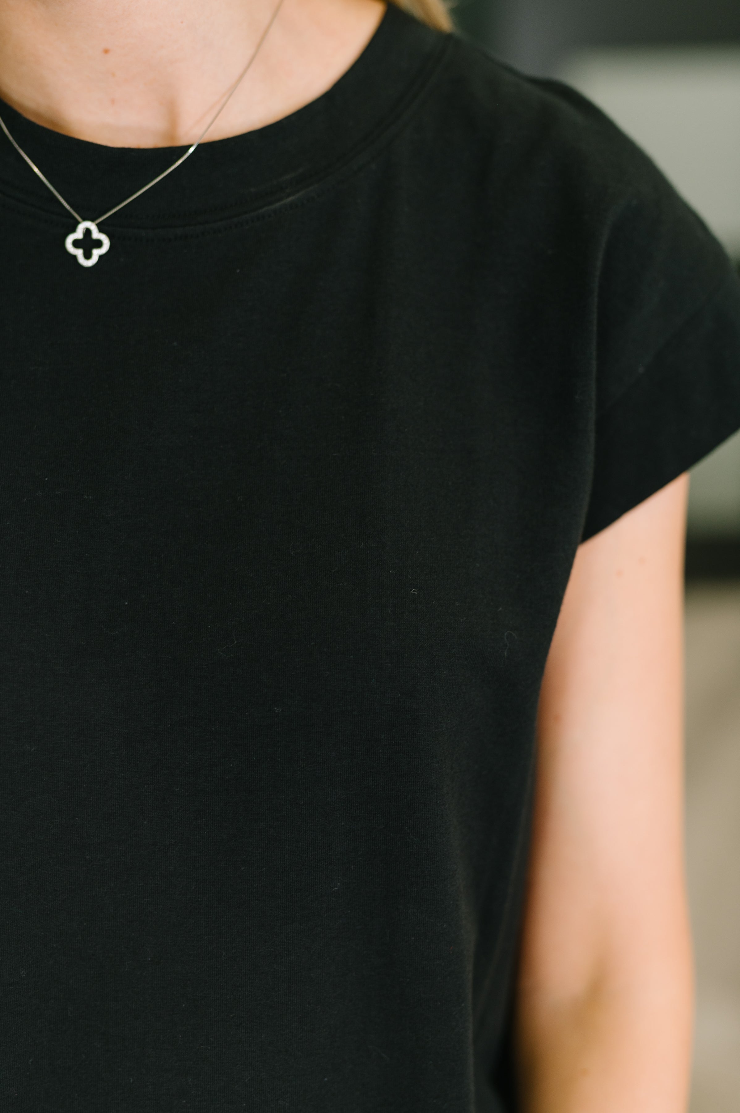 Close-up of black casual dress neckline and cap sleeve worn with delicate silver pendant necklace
