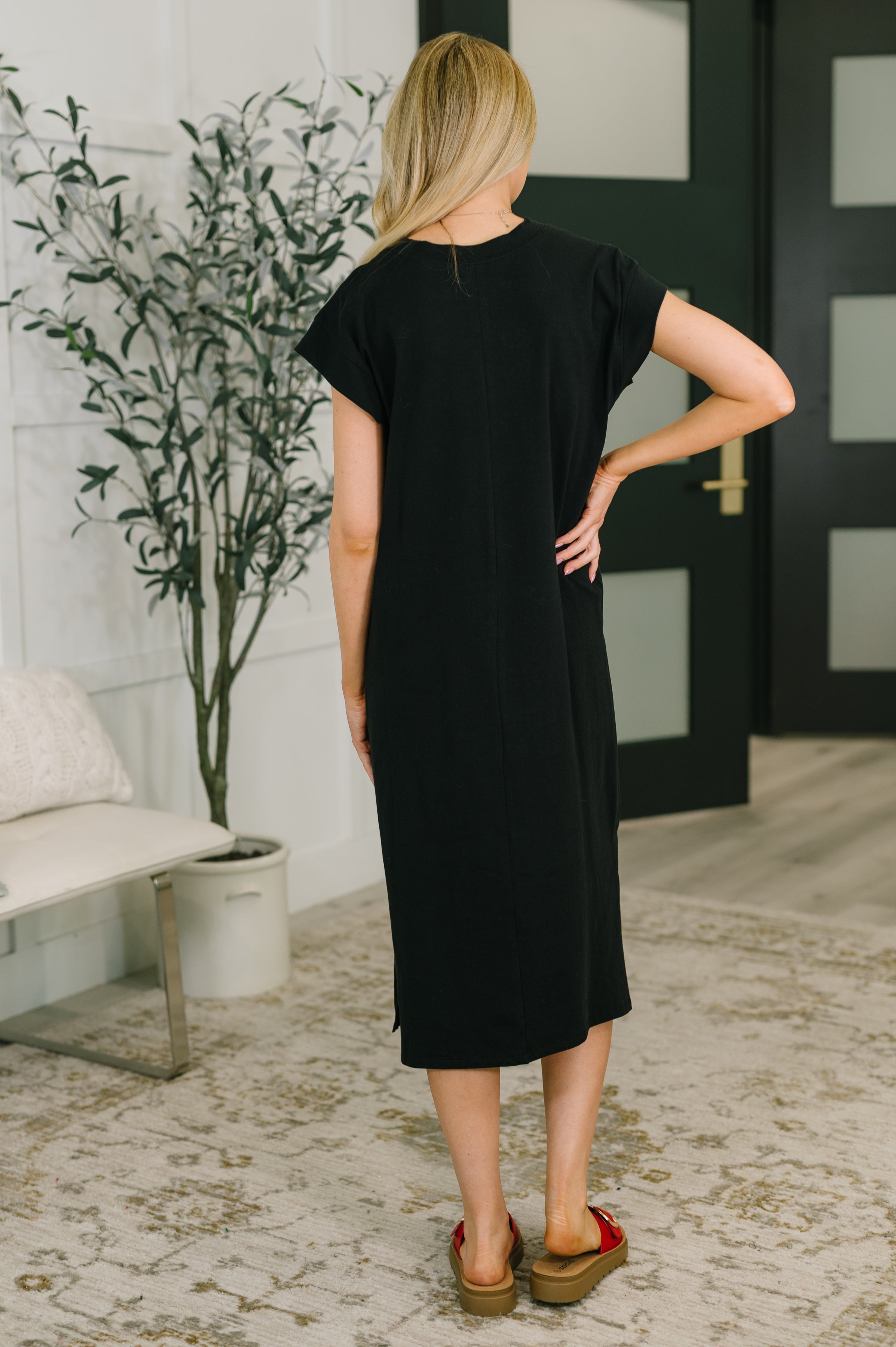 Woman seen from behind wearing a black casual midi dress with short sleeves and red platform sandals indoors