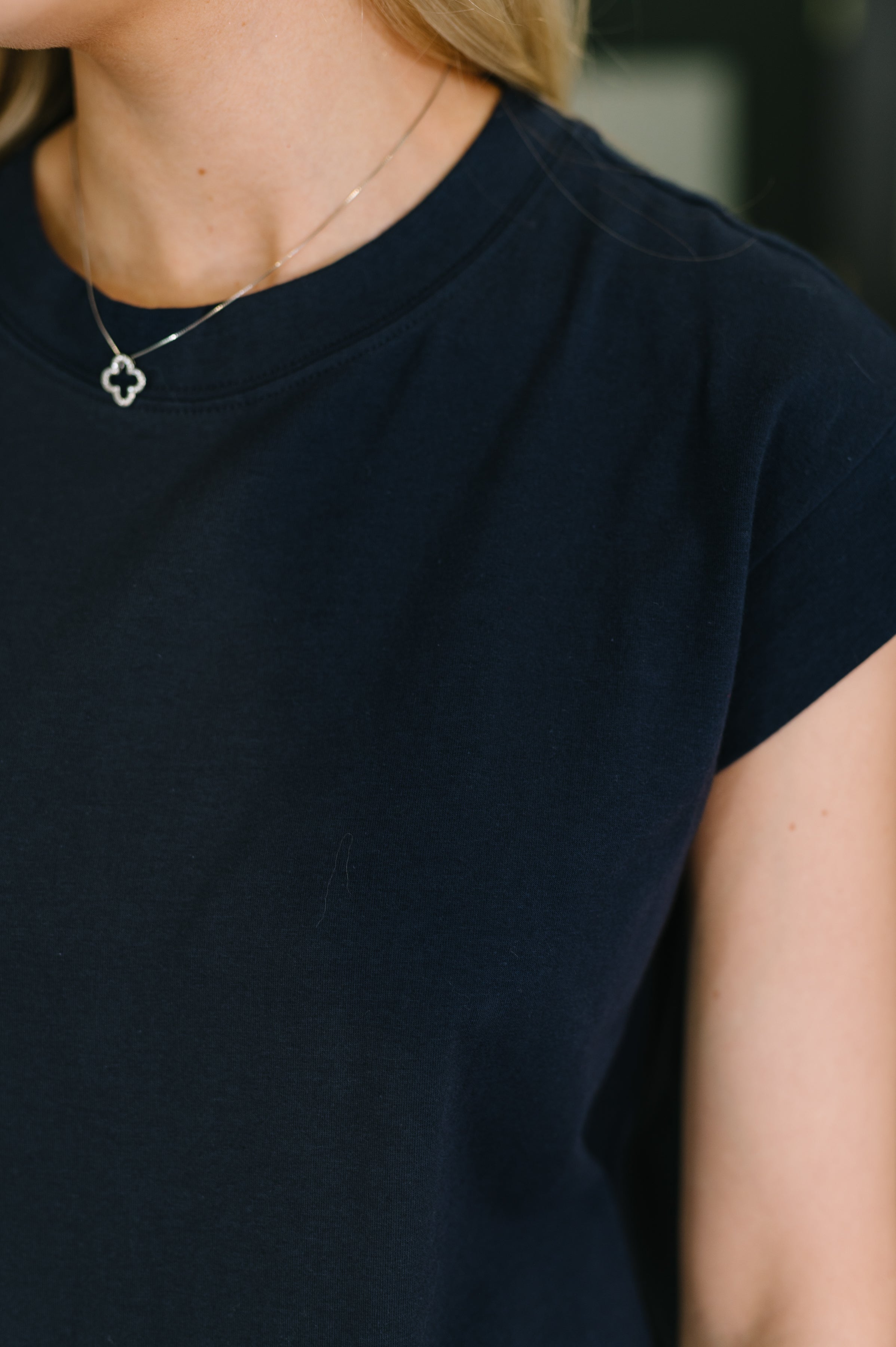 Close-up of navy blue casual dress fabric and short sleeve worn with delicate silver clover pendant necklace