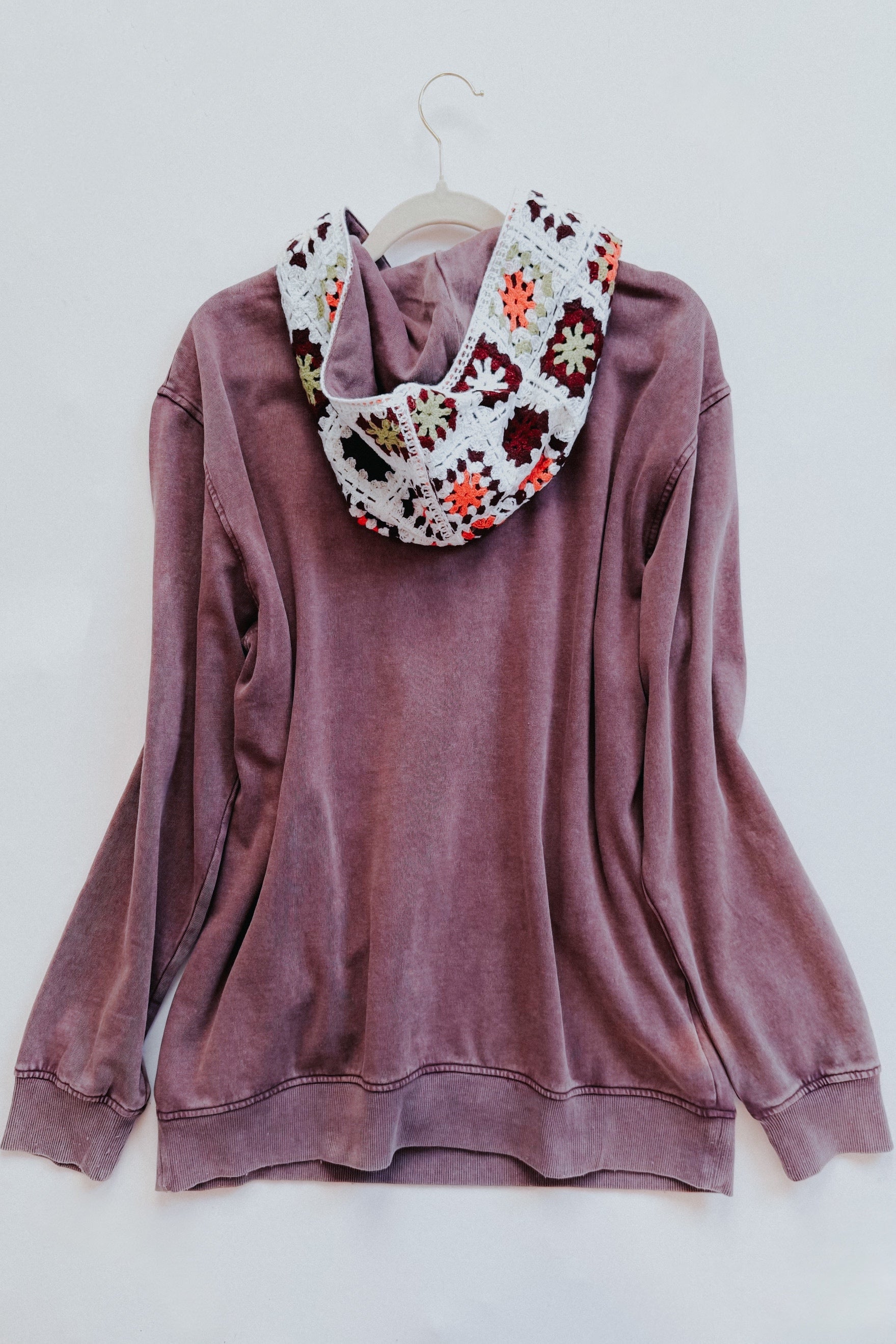 Purple acid wash hoodie with a colorful crochet hood hanging against a white background