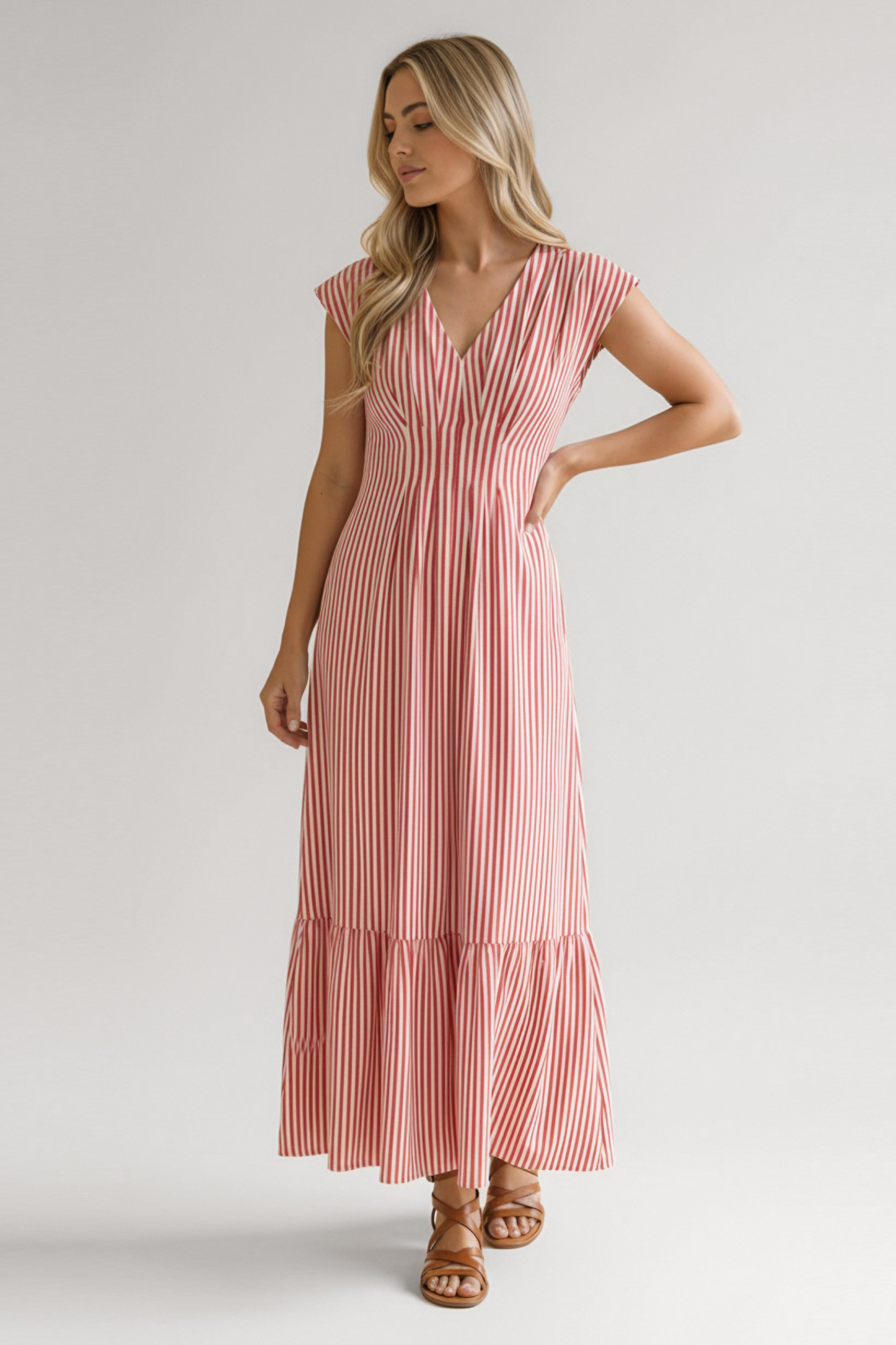 Woman wearing red striped tiered maxi dress with v-neck and cap sleeves paired with brown sandals standing against neutral background
