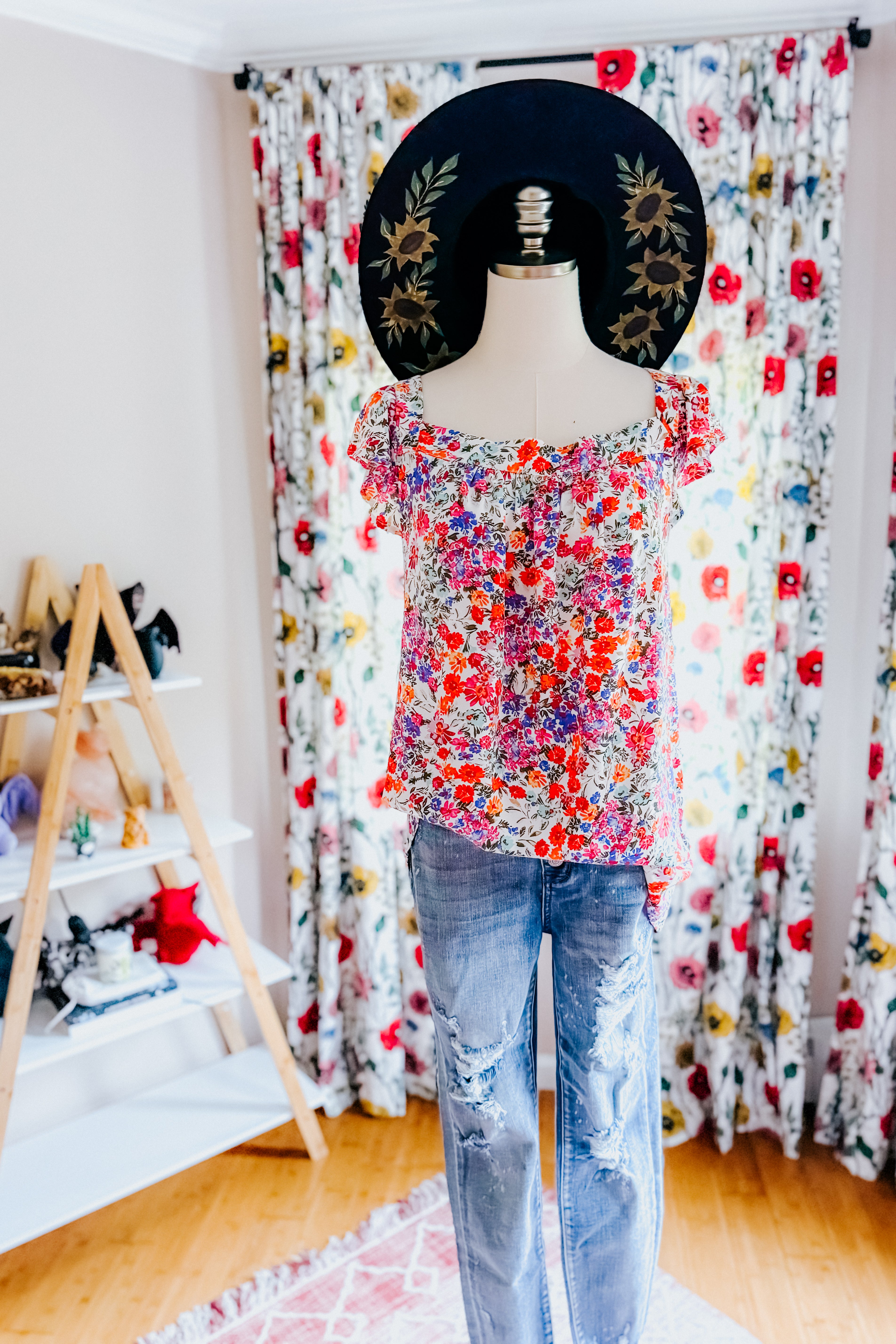 Mannequin dressed in a red floral square neck top paired with distressed blue jeans and a wide-brim hat with sunflower detailing