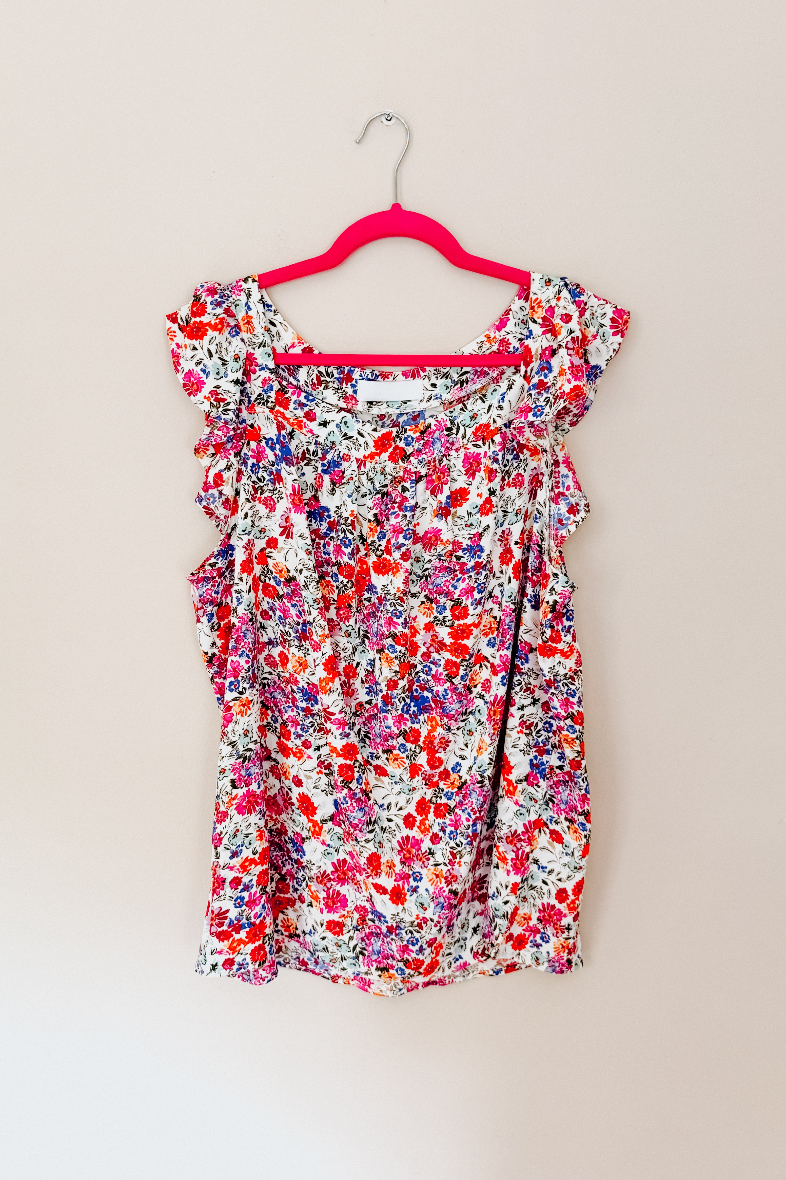 Red floral square neck top with flutter sleeves displayed on a pink hanger against a beige wall