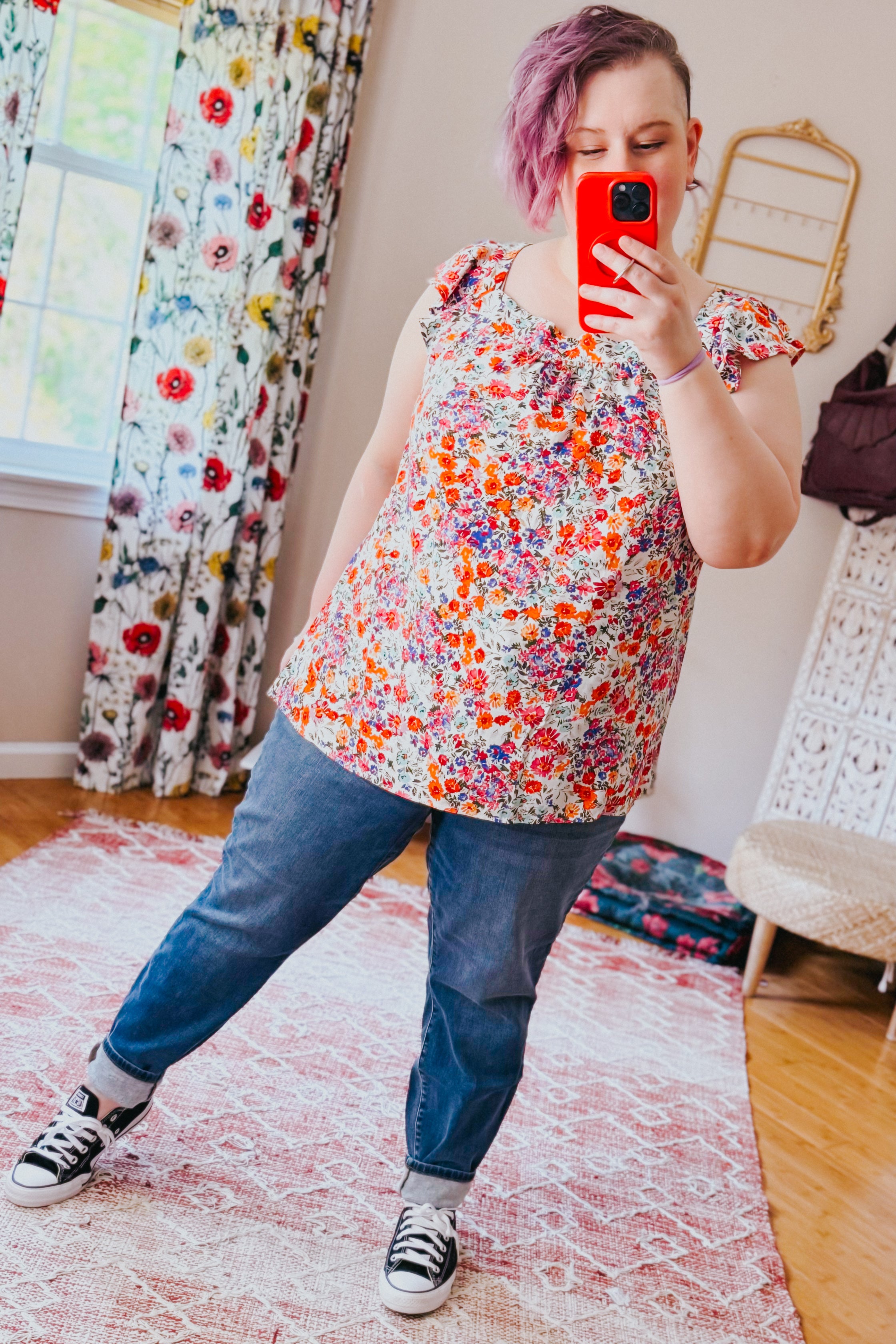 Woman wearing a red floral square neck top paired with rolled-up jeans and black sneakers indoors