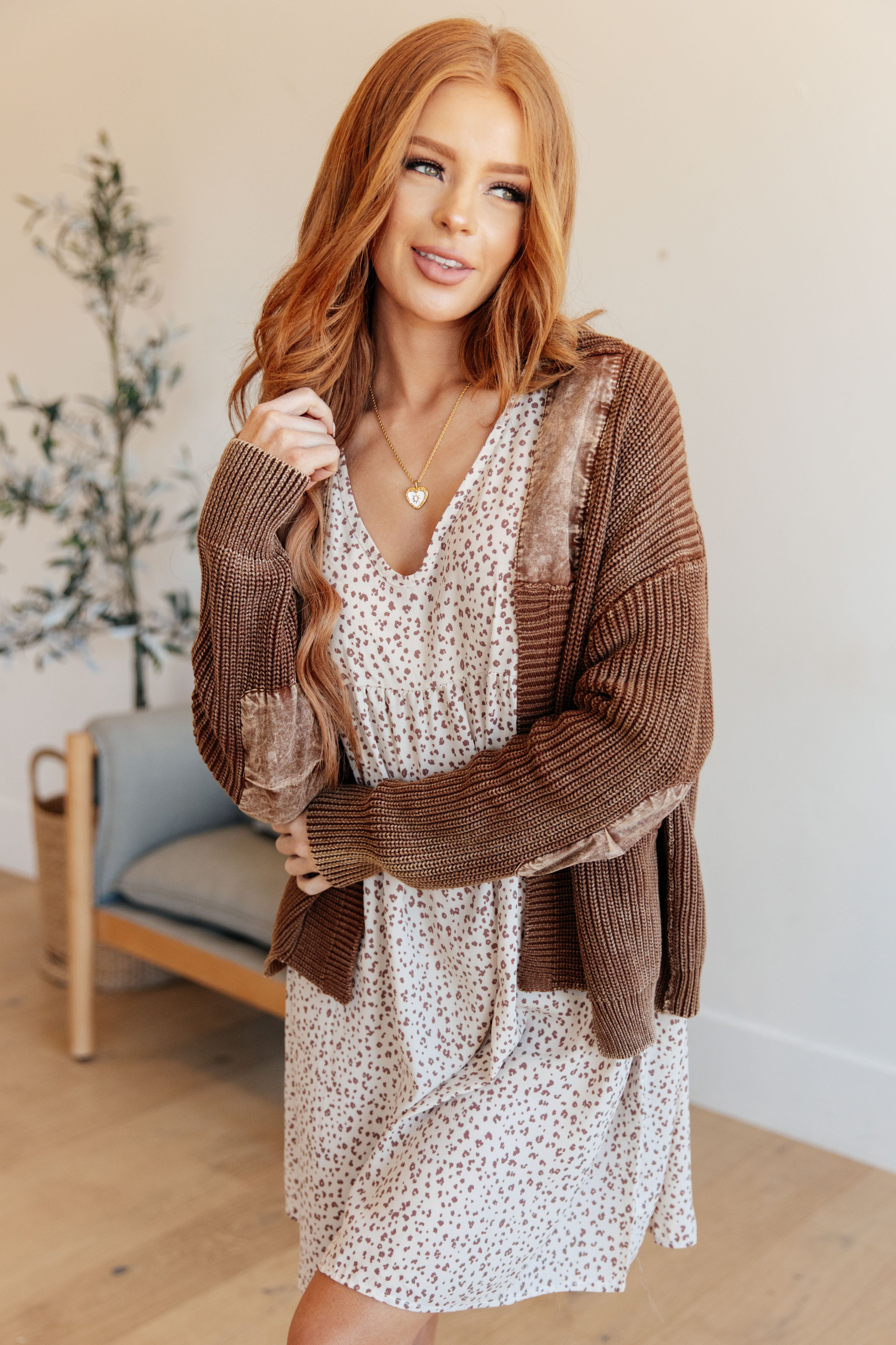 Woman with long hair wearing a cozy brown cardigan over a soft, floral patterned dress in a bright indoor space