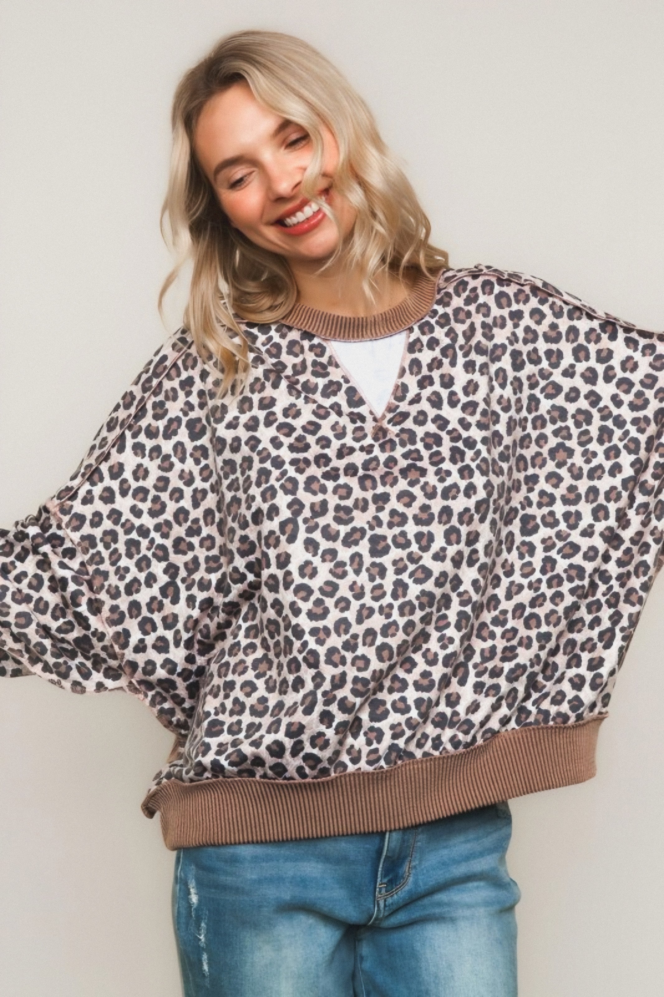 Smiling woman wearing a brown leopard-print pullover with ribbed trim and relaxed fit over casual blue jeans