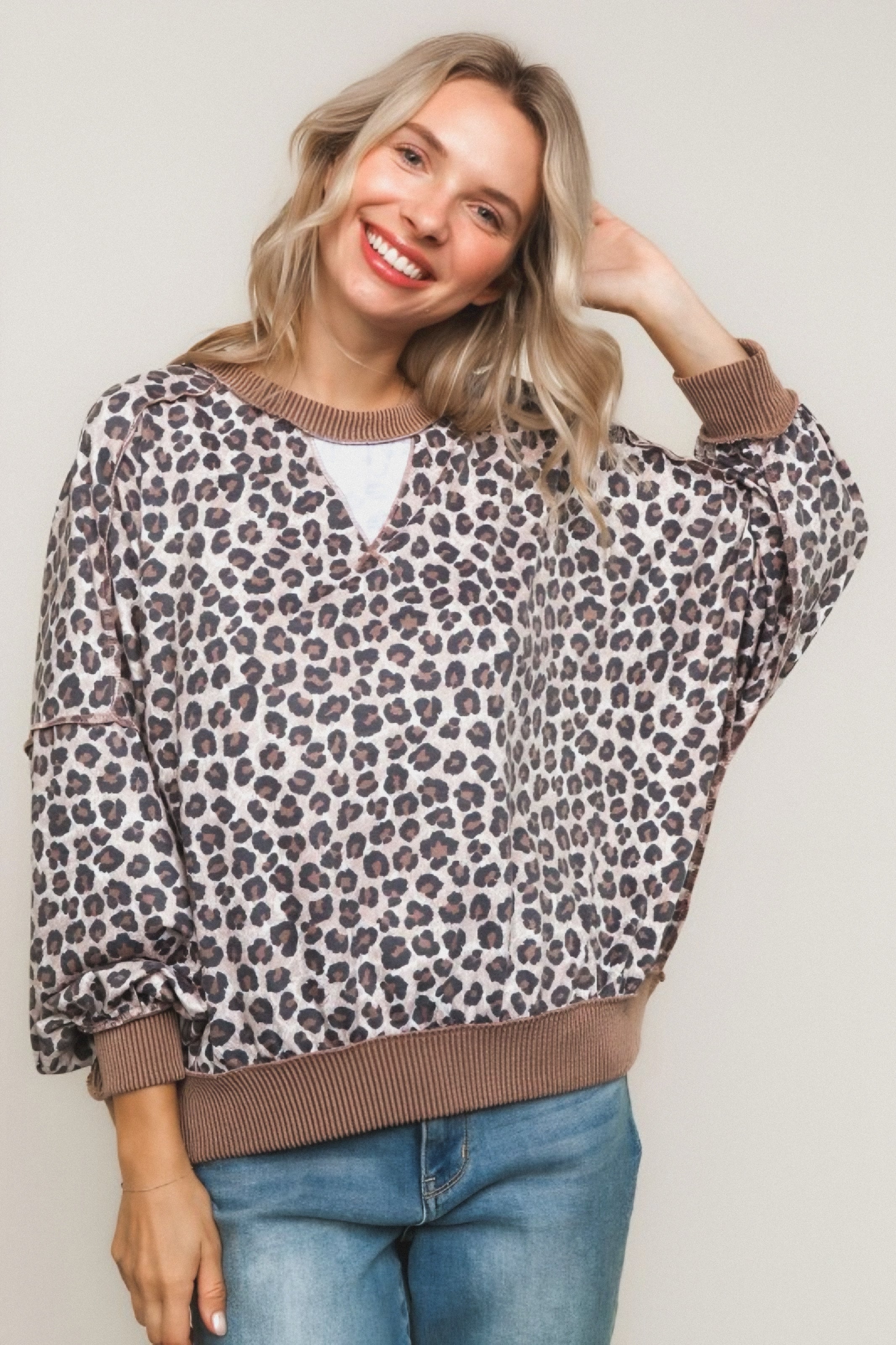 Smiling woman wearing a brown leopard print pullover with ribbed cuffs and hem paired with light blue jeans
