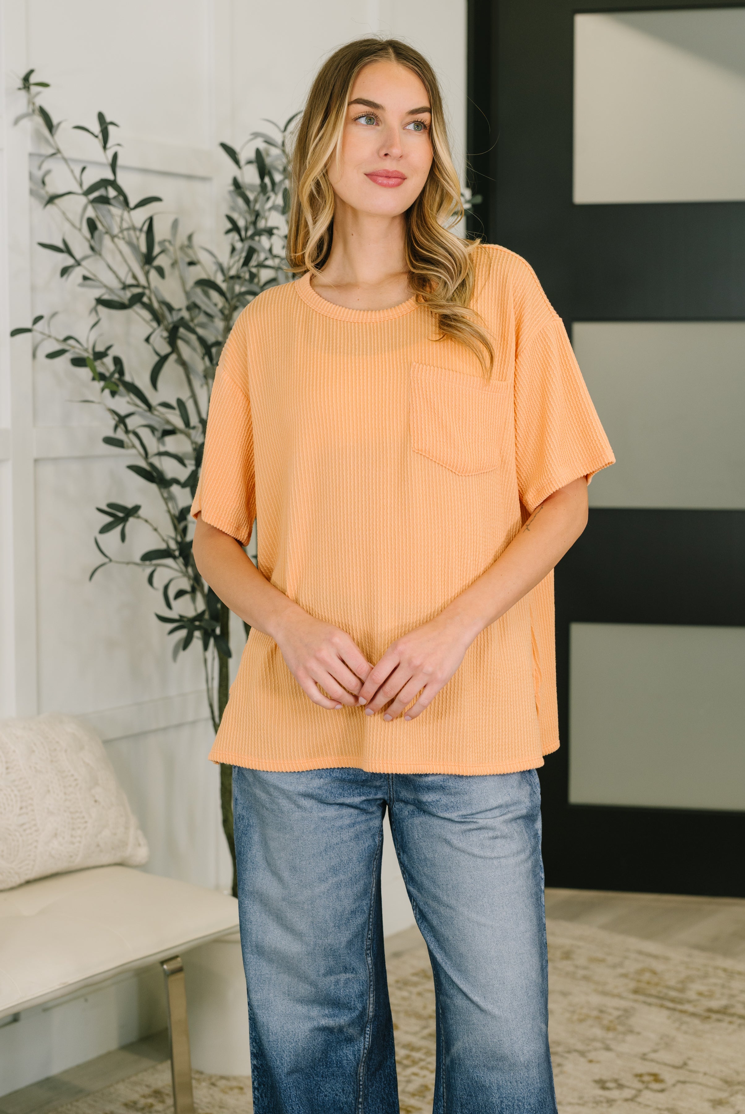 Woman wearing relaxed fit apricot ribbed tee with pocket paired with wide-leg blue jeans indoors