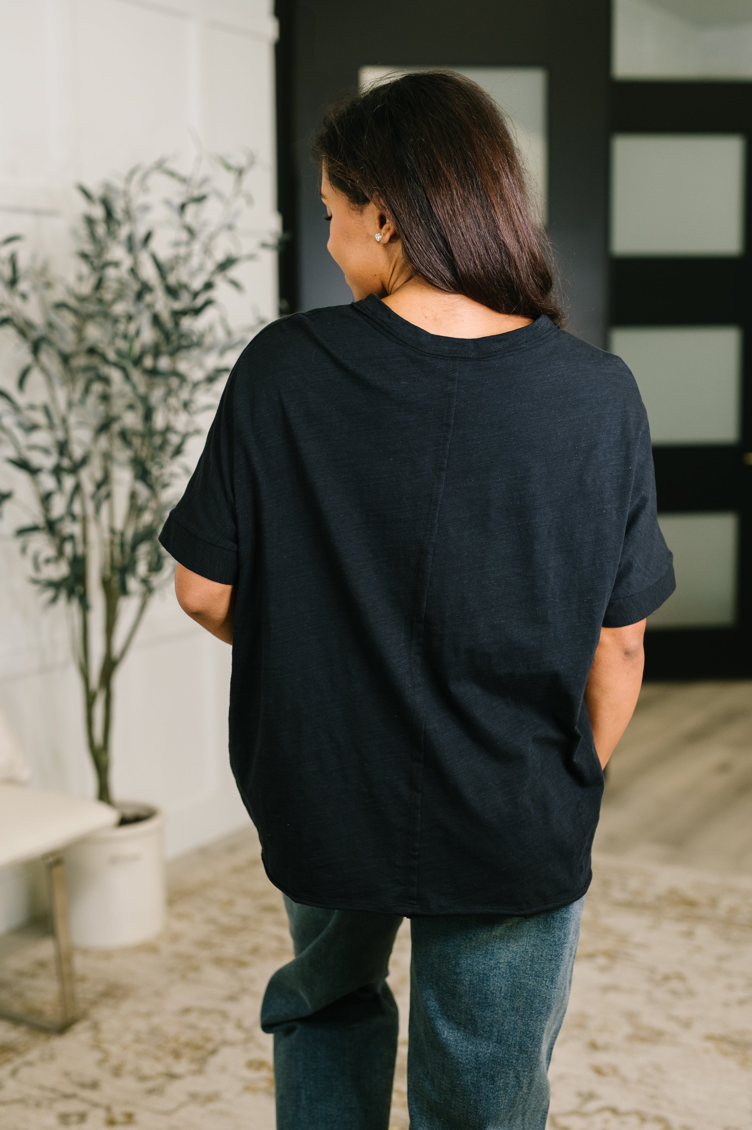 Back view of woman wearing loose black relaxed tee with rolled sleeves paired with blue jeans indoors