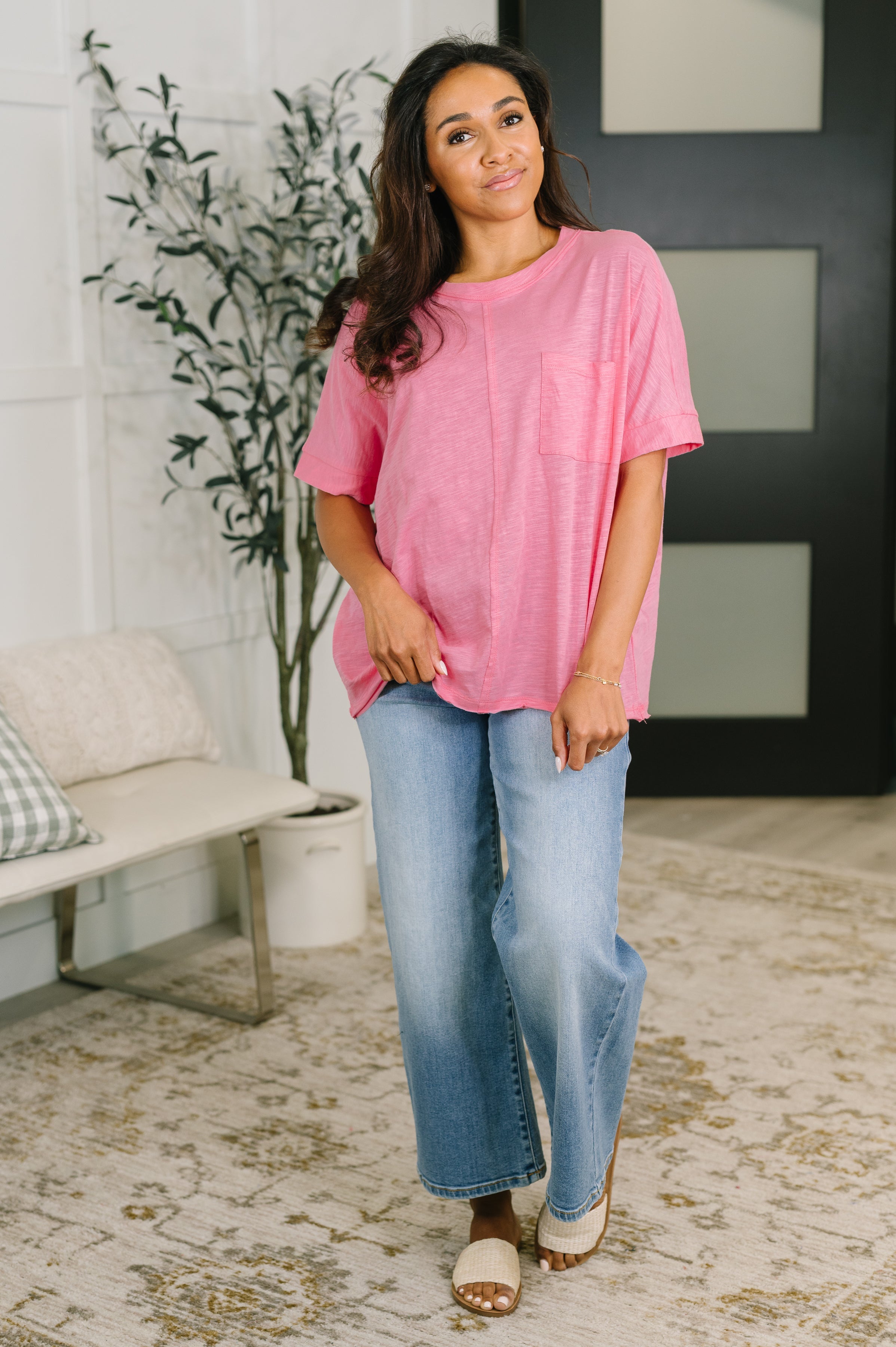 Woman wearing relaxed pink boxy tee with light blue wide-leg jeans and slip-on sandals indoors
