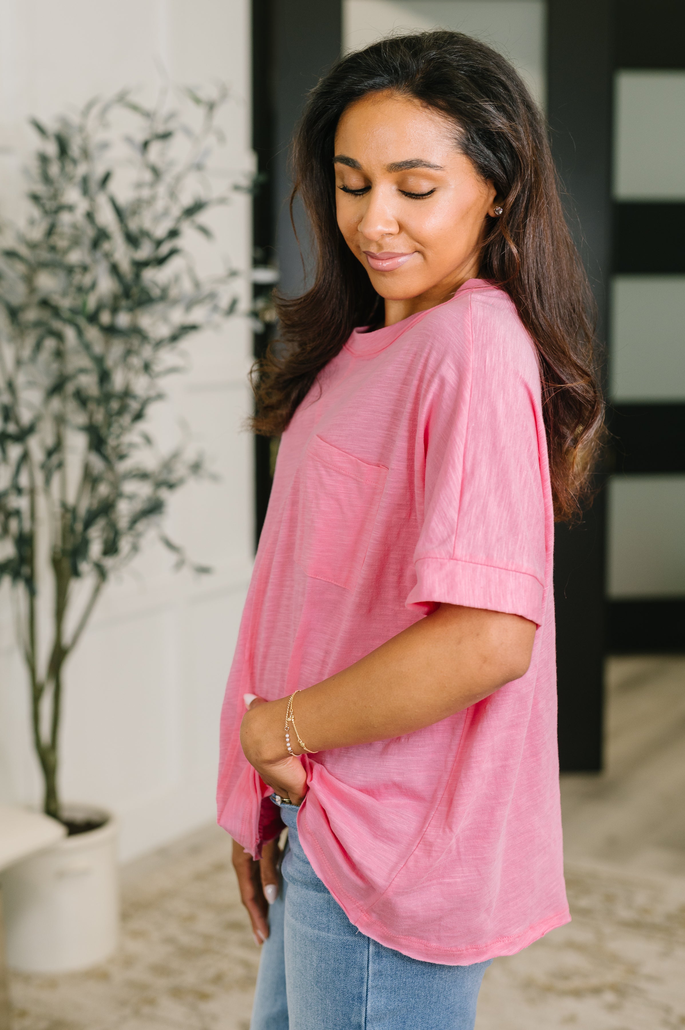 Woman wearing soft pink relaxed fit tee with rolled sleeves and front pocket standing indoors near plant