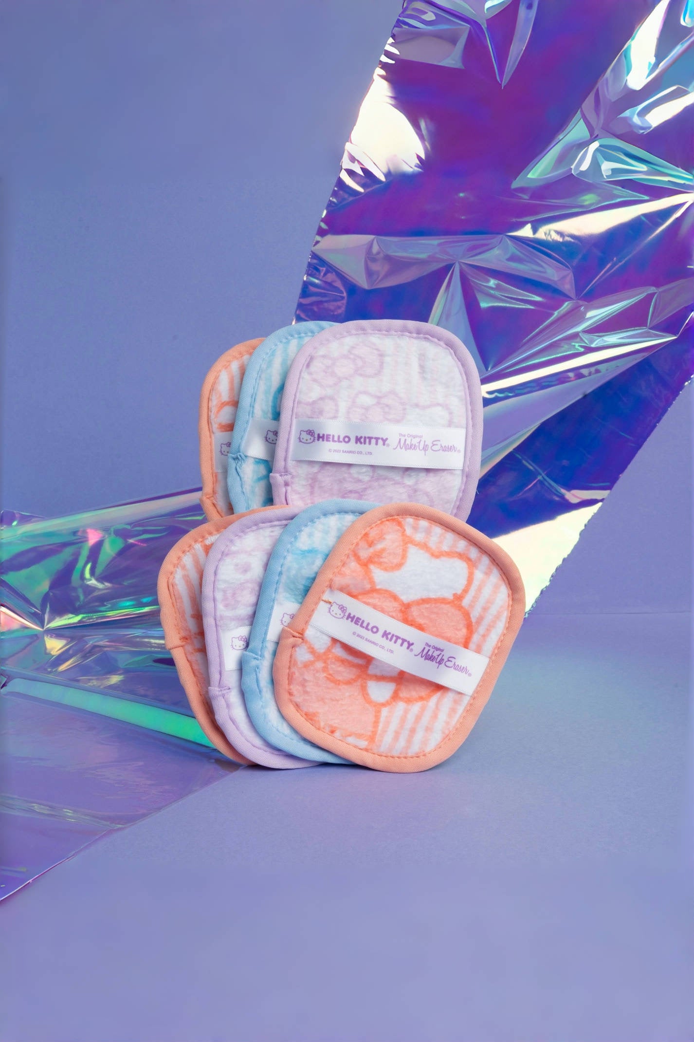 Set of soft makeup eraser pads in orange, blue, and purple tones with Hello Kitty design on iridescent background