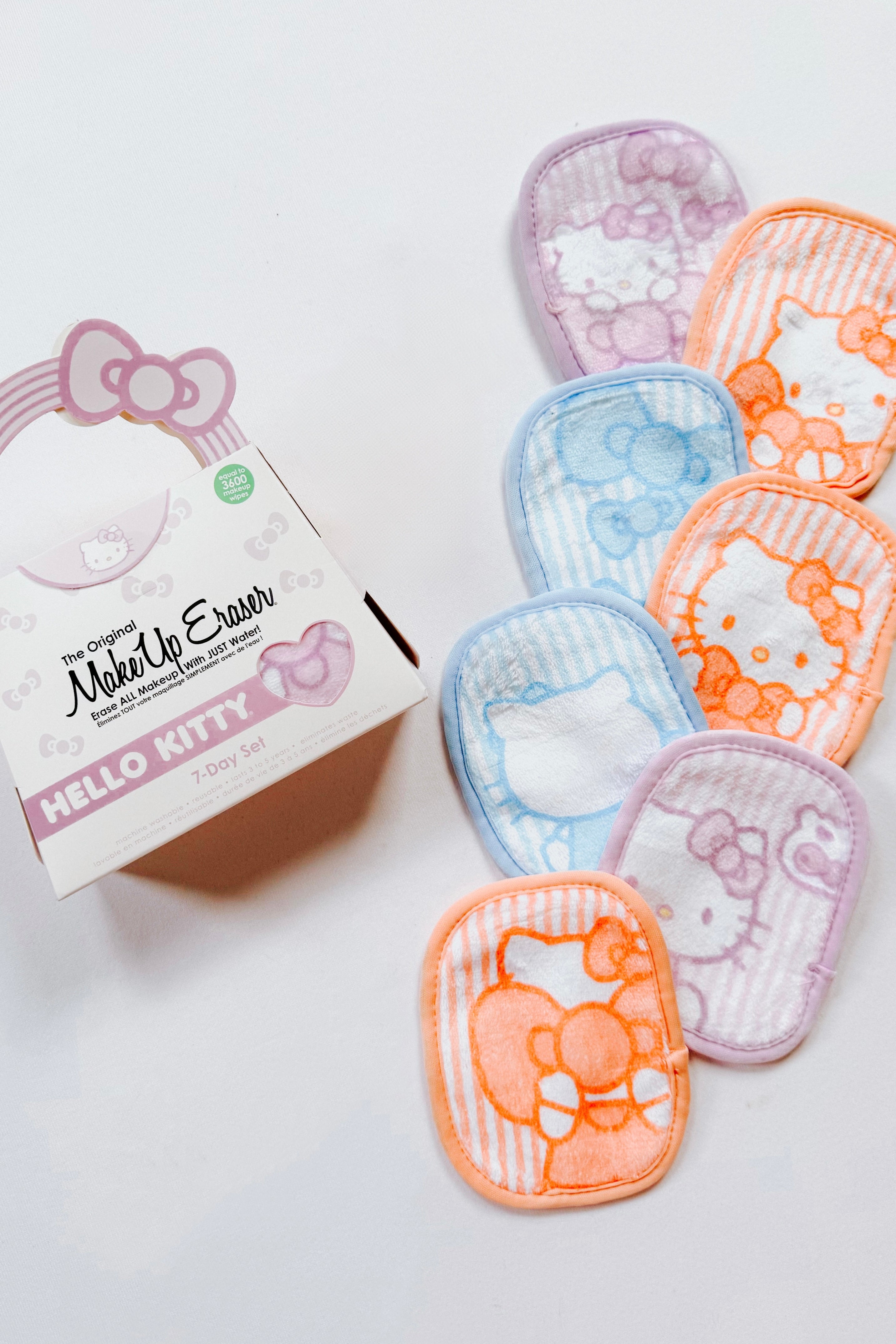 Seven pastel-colored makeup remover cloths with Hello Kitty designs arranged beside a themed gift box on white background