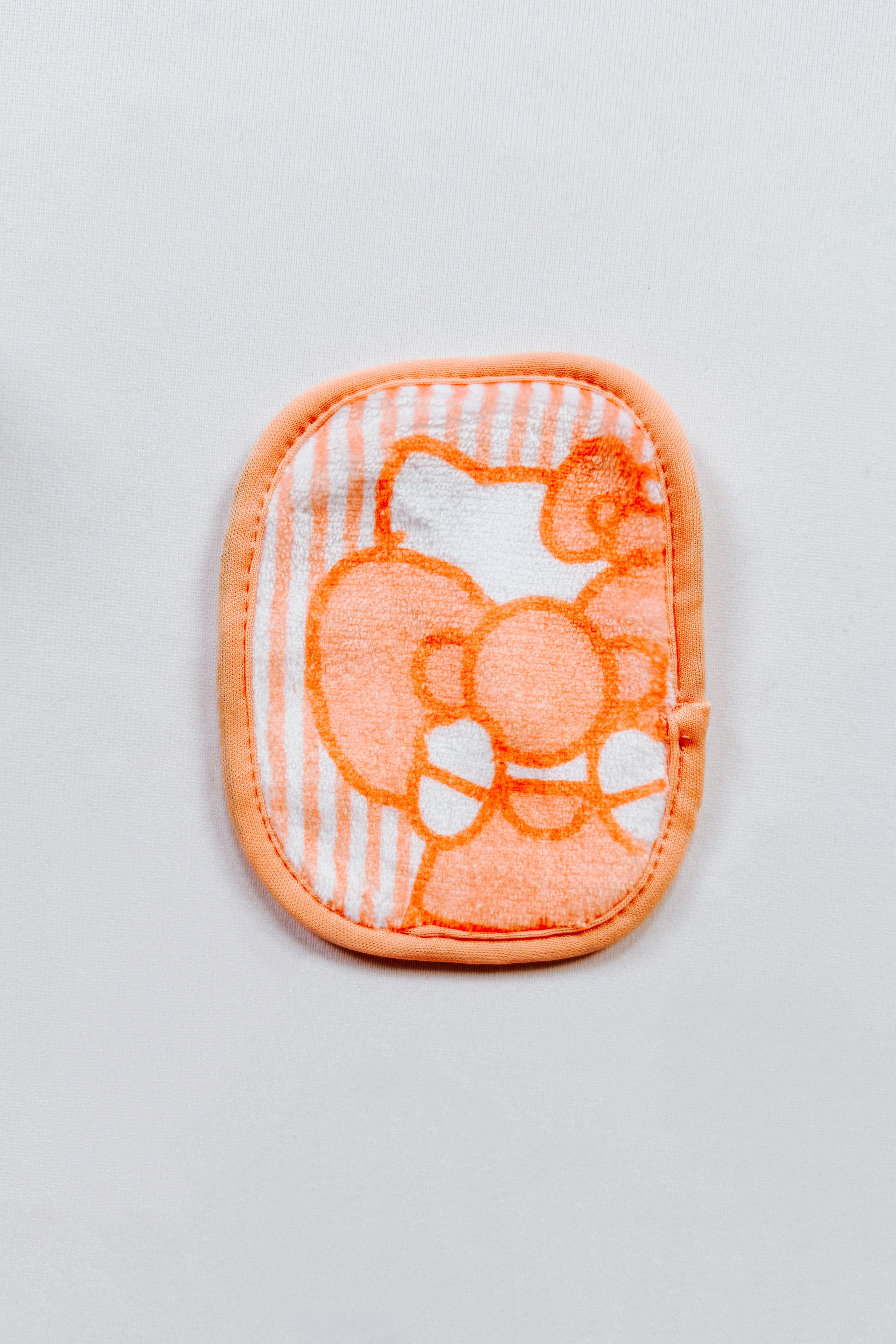 Small orange and white makeup eraser cloth featuring a playful Hello Kitty design on a soft striped background