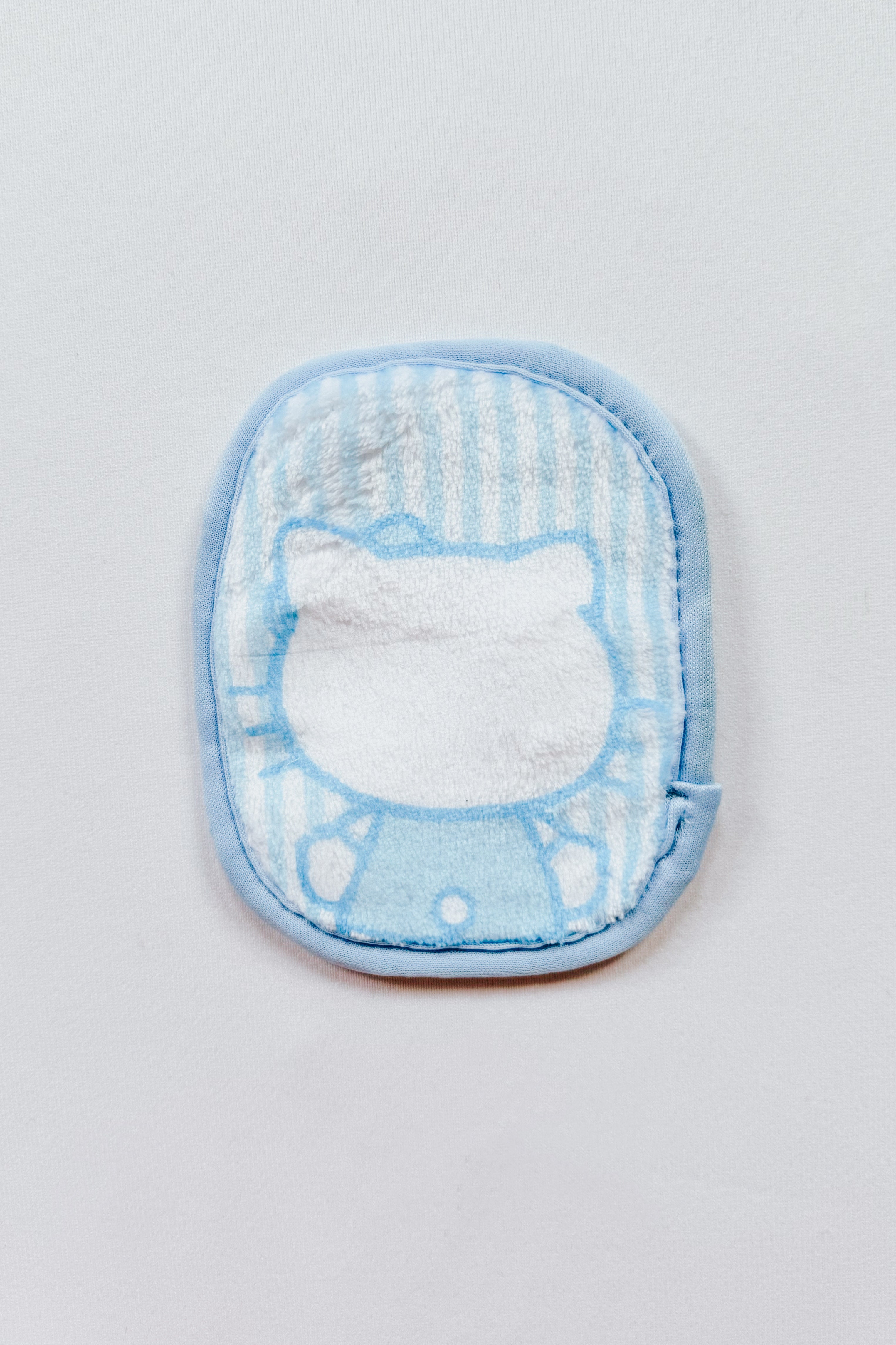 Small blue and white makeup eraser cloth with cartoon character outline on light background